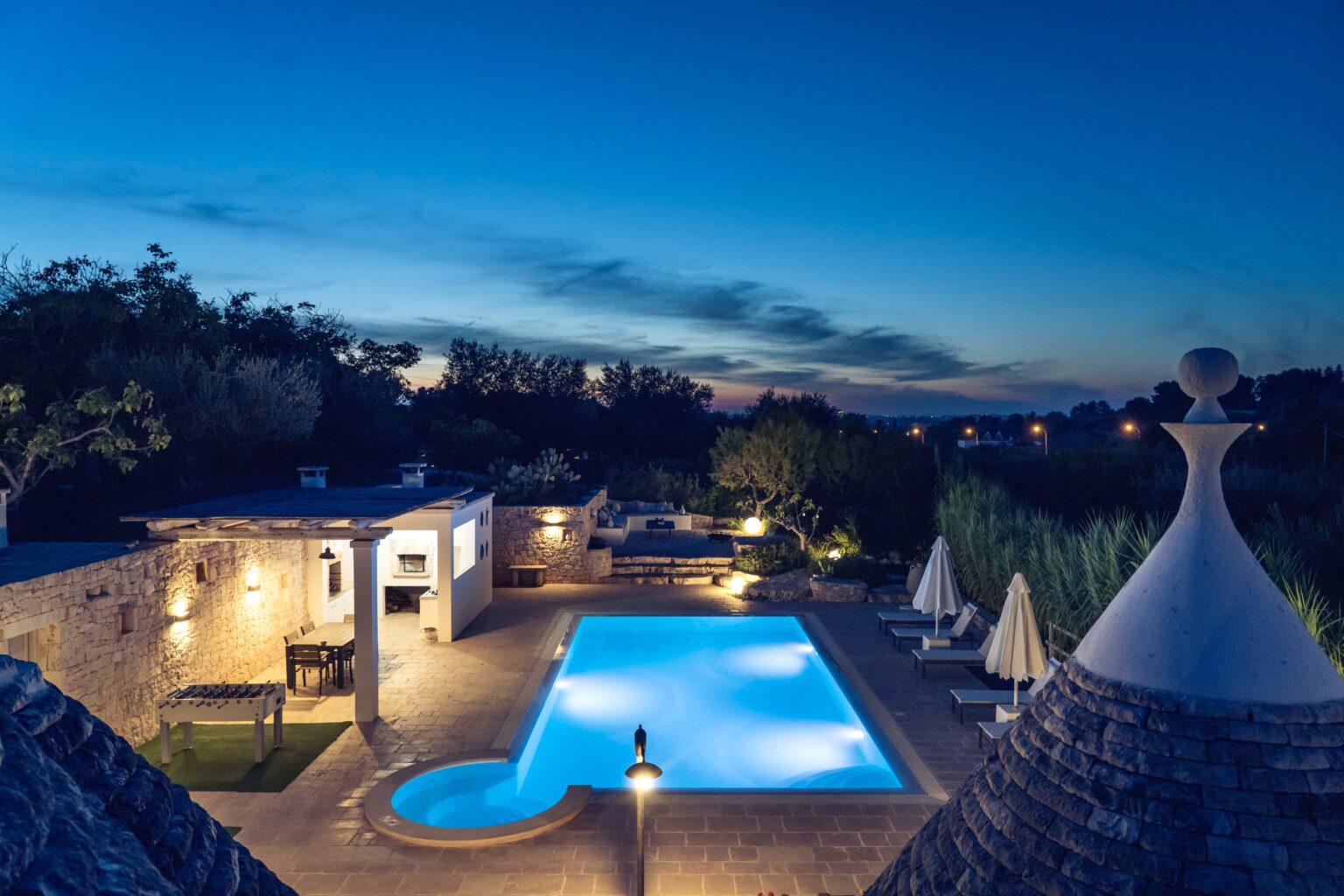 Luxury villa with a swimming pool at dusk, featuring cozy seating areas and lush greenery, creating a serene atmosphere. | Only on SopranoVillas