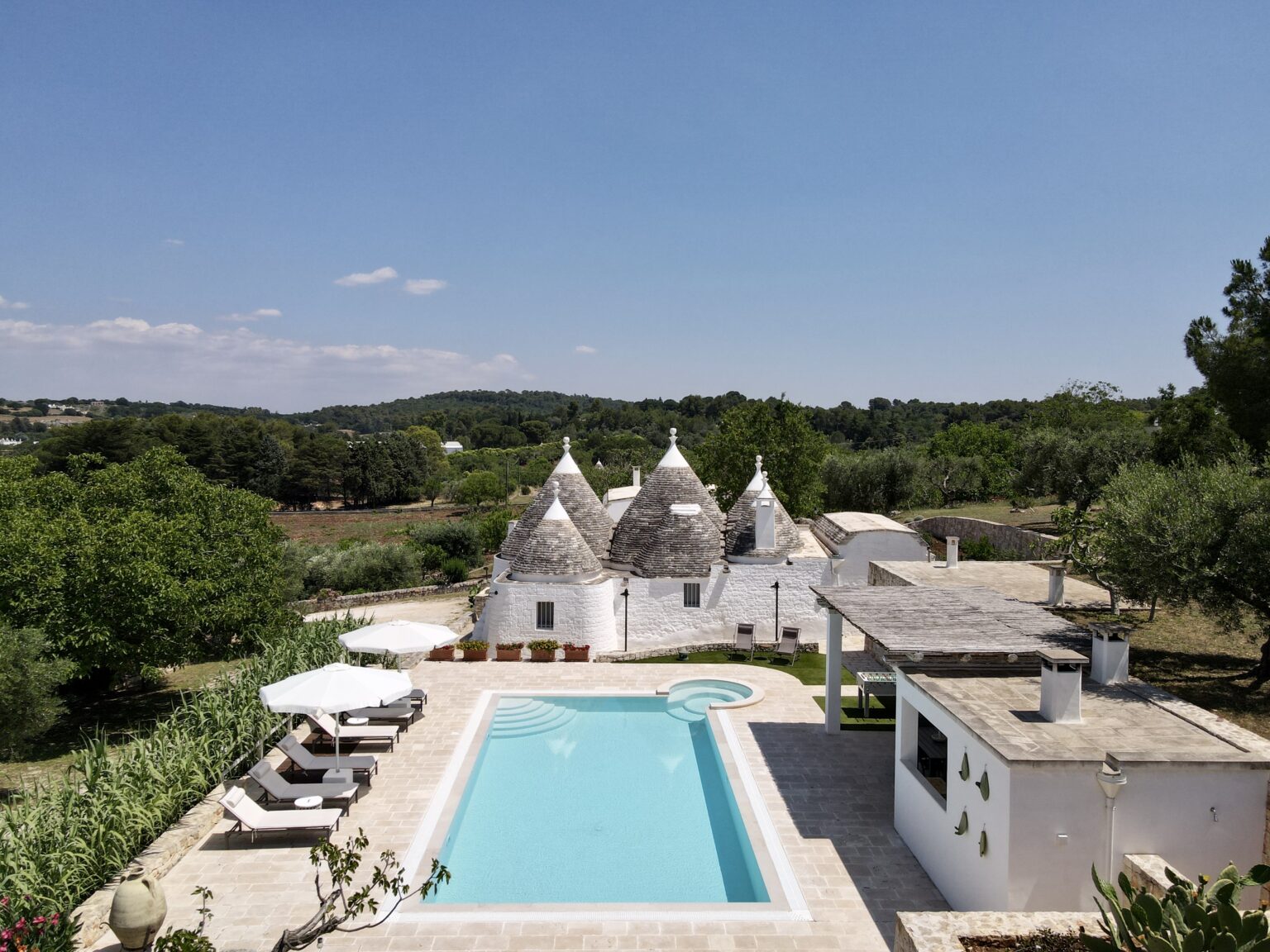 Tranquil villa with traditional trulli architecture, surrounded by lush greenery and featuring a sparkling swimming pool, ideal for a relaxing getaway in the Italian countryside. | Only on SopranoVillas