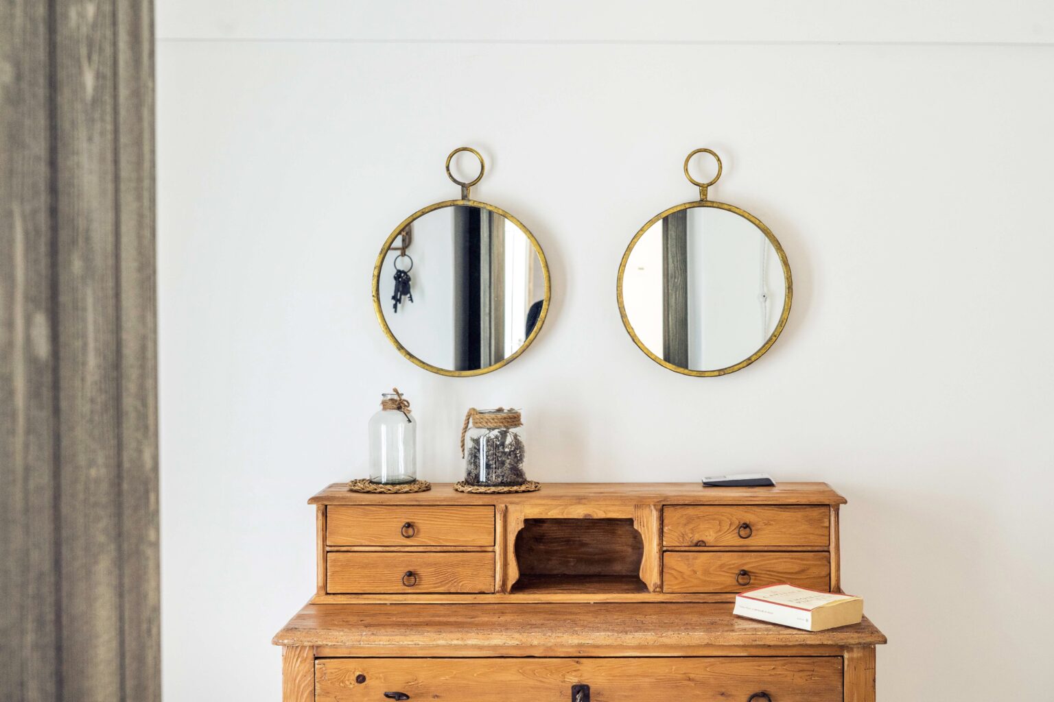 Wooden dresser with multiple drawers and decorative items, featuring two round mirrors with gold frames mounted on a white wall. | Only on SopranoVillas