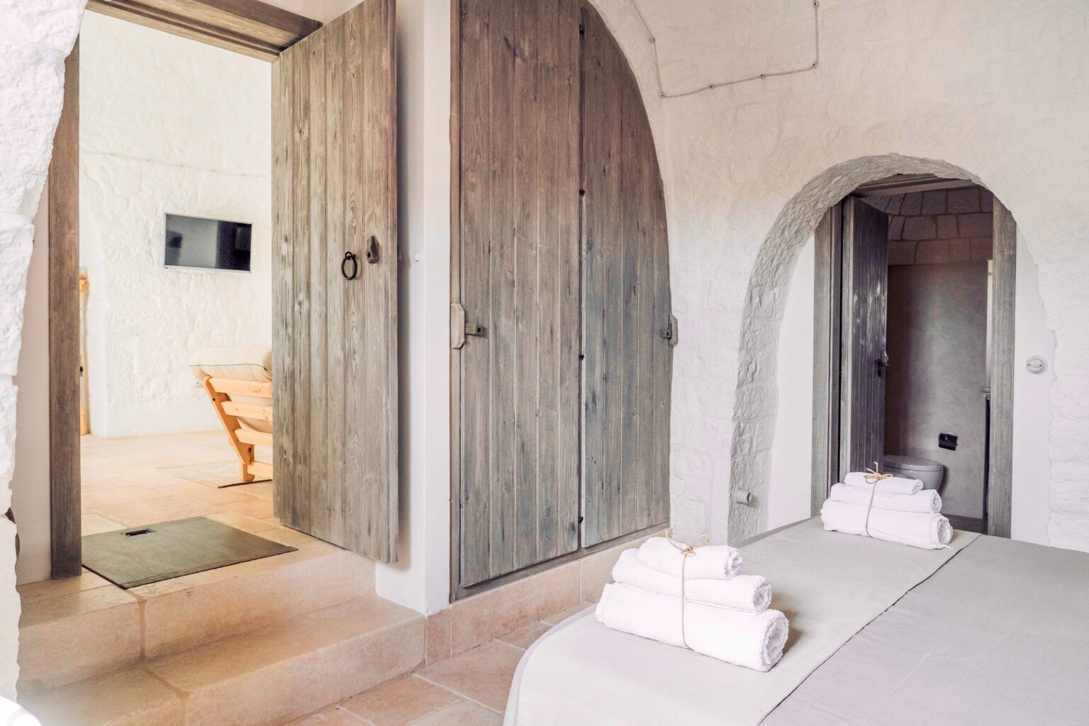Cozy interior of a spa room featuring wooden doors, a minimalist design, and neatly arranged towels on a massage bed, creating a serene atmosphere for relaxation. | Only on SopranoVillas