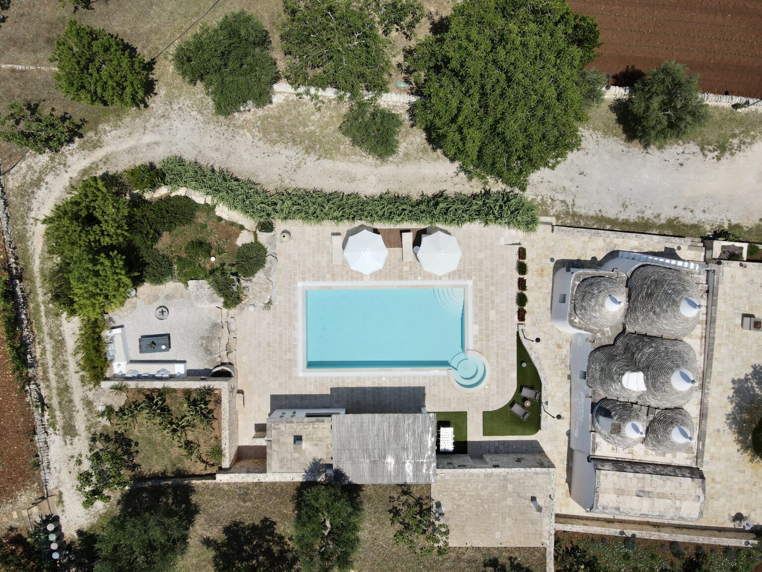 Aerial view of a modern villa featuring a rectangular swimming pool surrounded by lounge areas, sun umbrellas, and landscaped gardens, showcasing a tranquil outdoor retreat. | Only on SopranoVillas