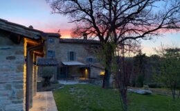 Scenic view of a rustic stone villa at sunset, surrounded by lush greenery and trees, showcasing a warm, inviting atmosphere with soft lighting illuminating the exterior.