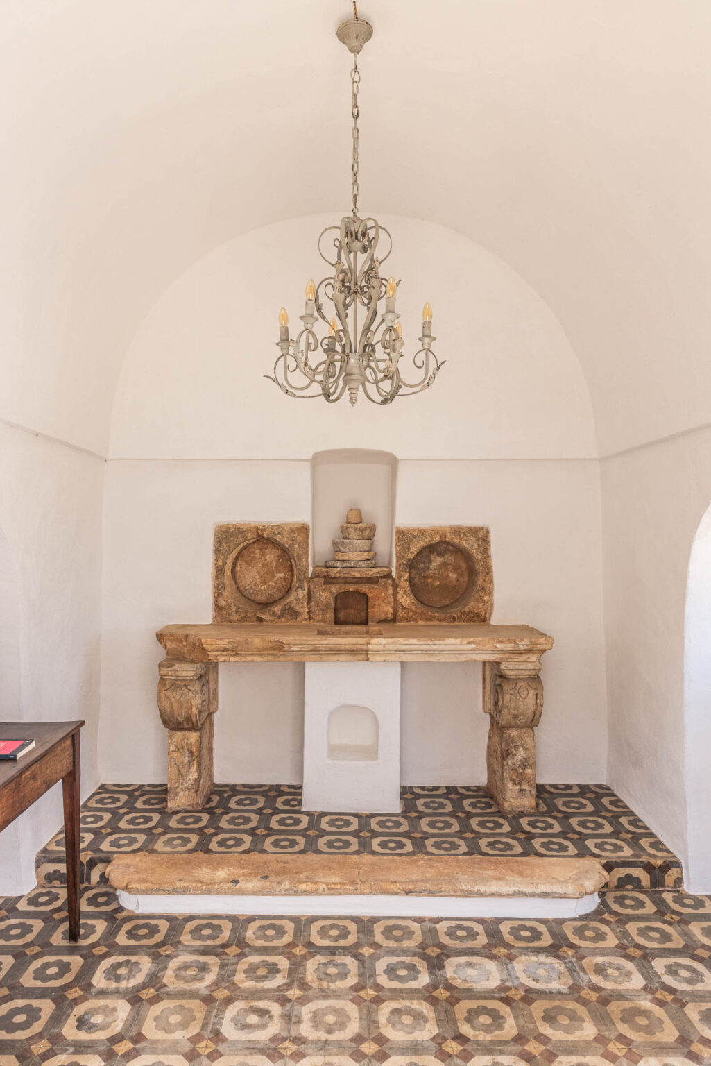 Interior view of a serene space featuring a wooden altar with decorative stone elements, an intricate chandelier hanging from a vaulted ceiling, and patterned tile flooring, creating a tranquil atmosphere. | Only on SopranoVillas