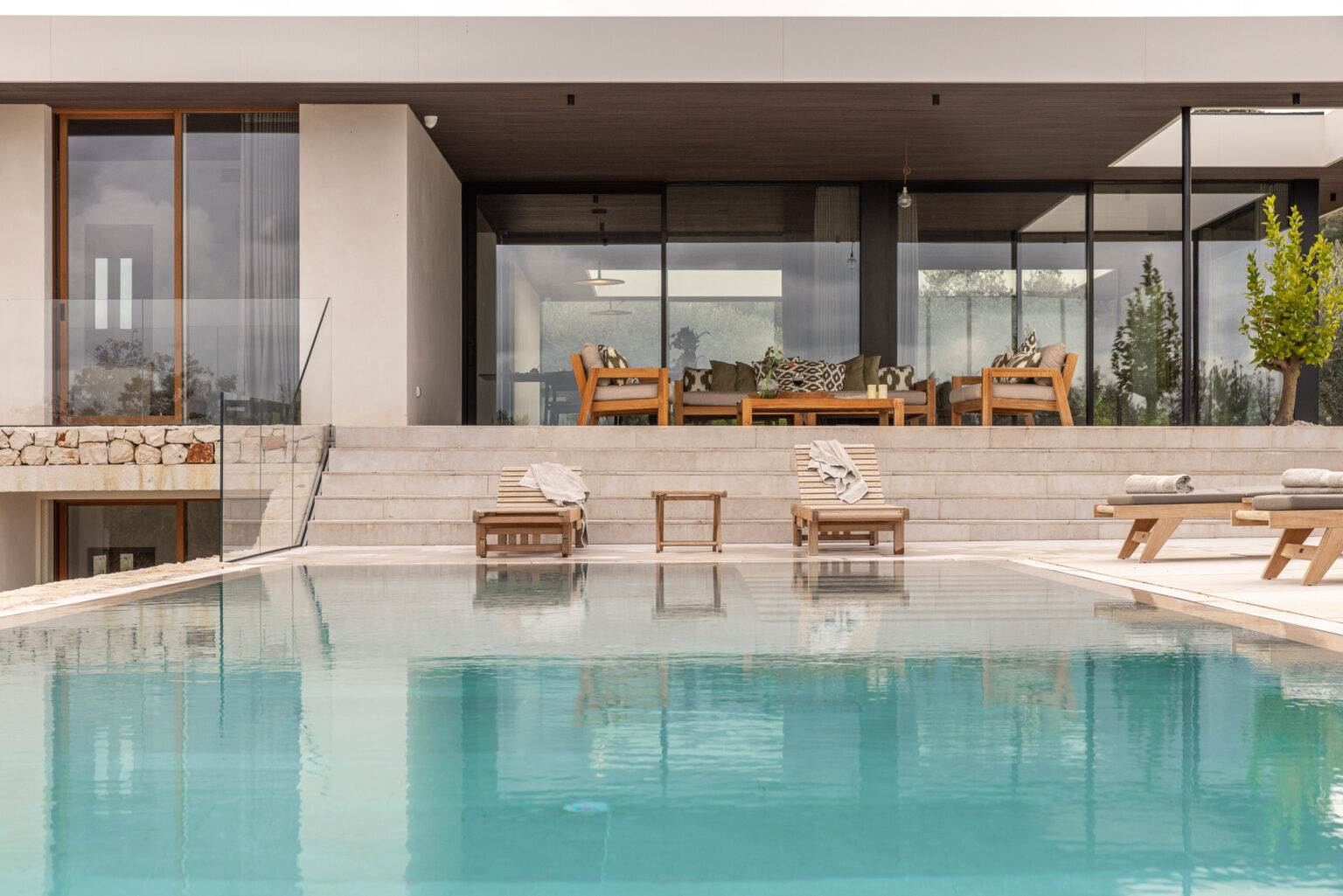 Modern luxury villa with a swimming pool, featuring a spacious outdoor terrace and stylish wooden furniture, surrounded by greenery. | Only on SopranoVillas