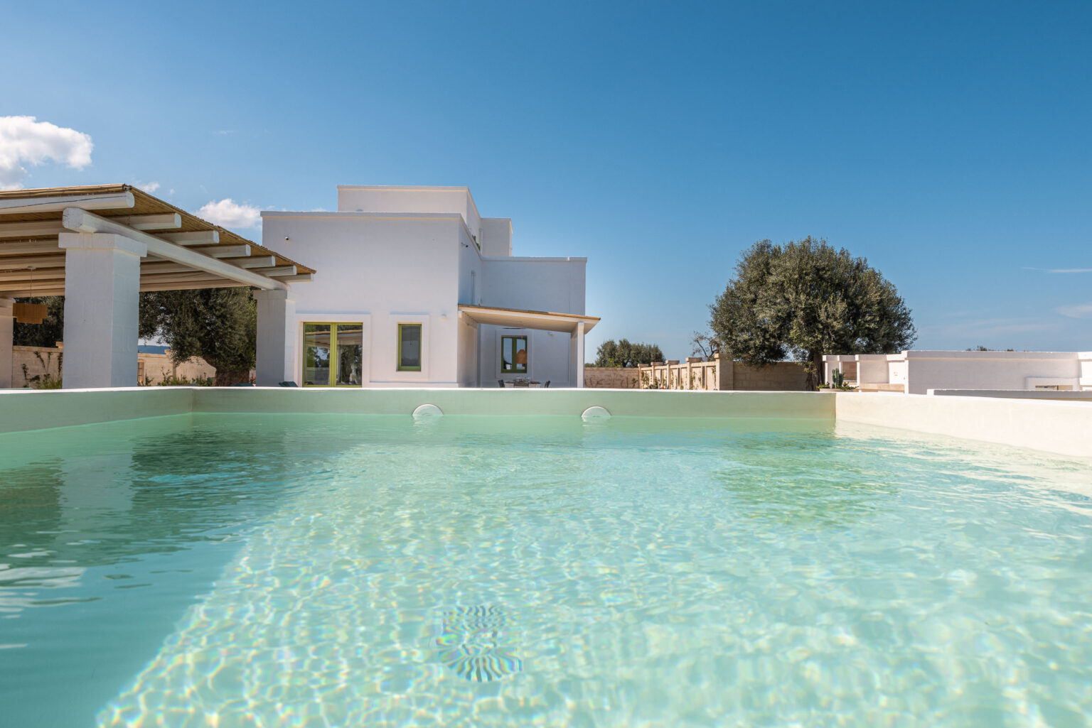 Modern villa with a clear swimming pool under a blue sky, featuring a spacious outdoor area and lush greenery. Ideal for luxury vacation rentals and relaxation. | Only on SopranoVillas