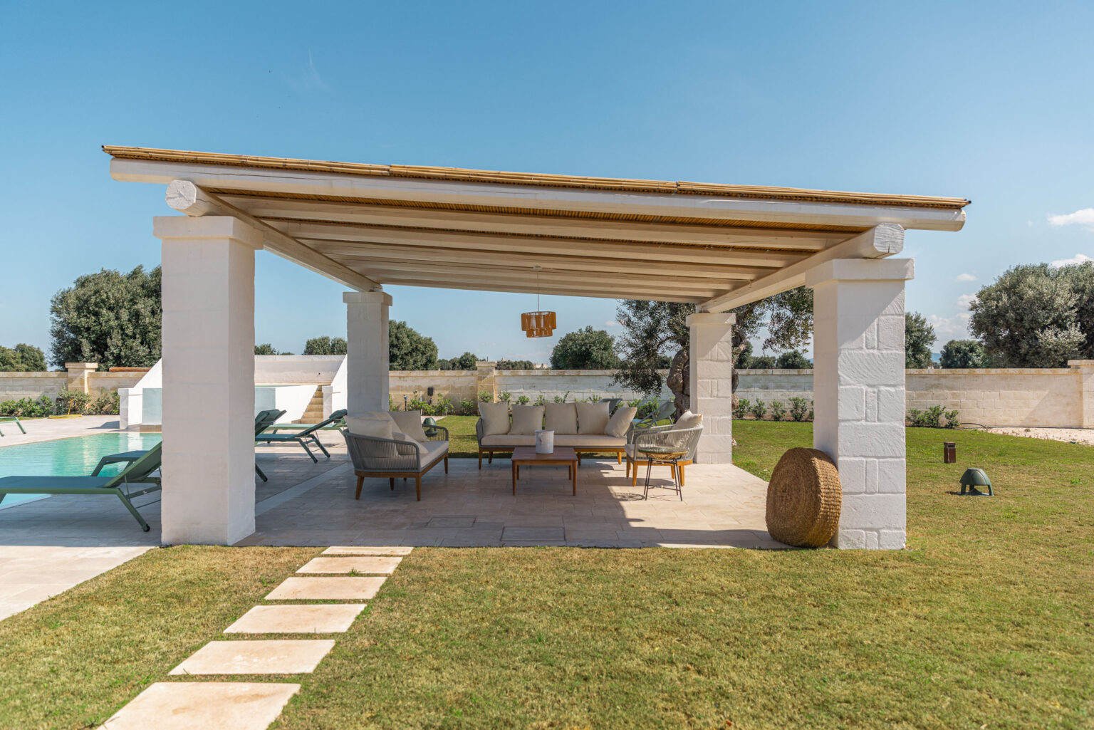 Outdoor patio with a wooden pergola, featuring comfortable seating and a view of a swimming pool surrounded by lush greenery. Ideal for relaxation and entertaining. | Only on SopranoVillas