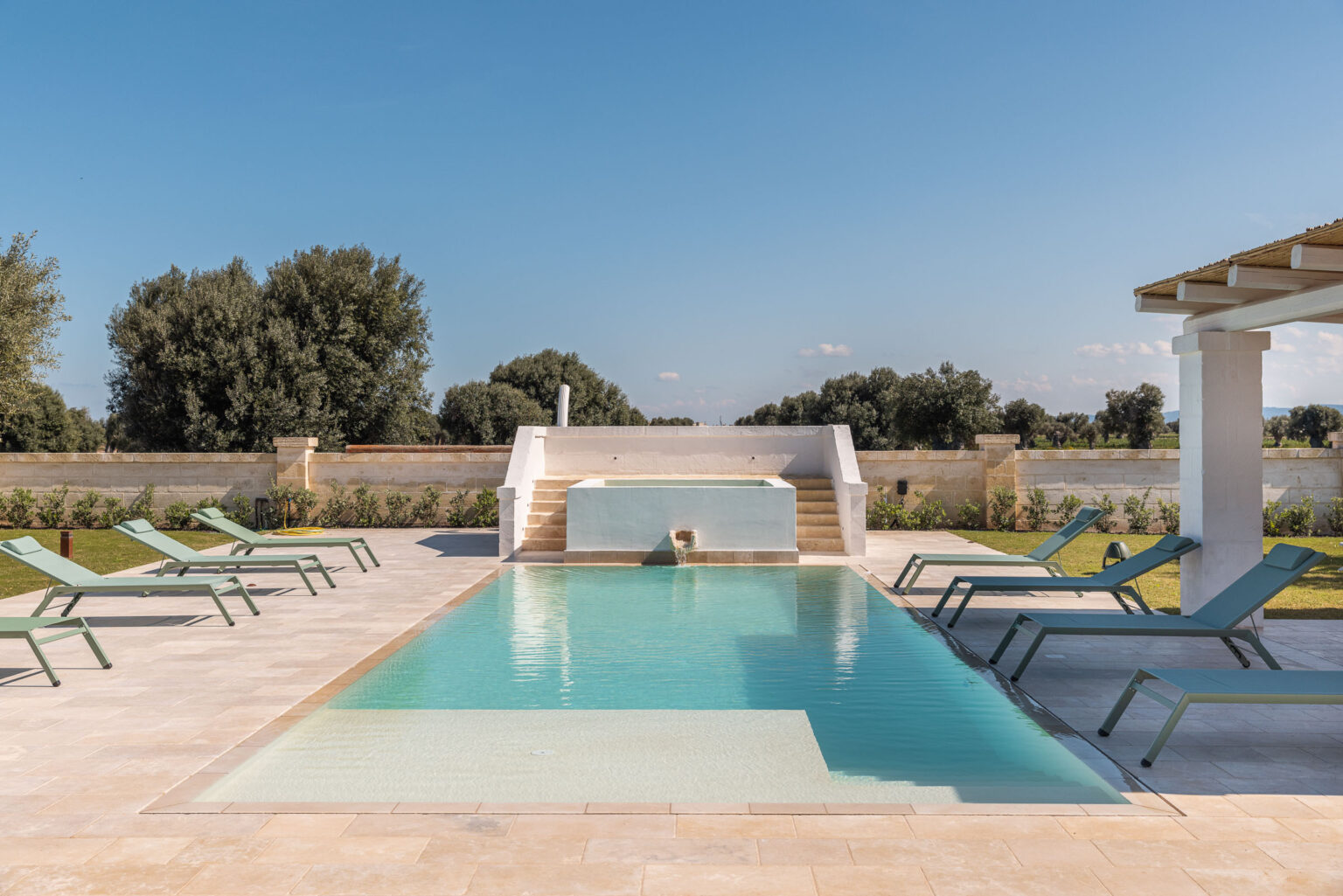 Modern outdoor swimming pool with lounge chairs, surrounded by greenery and blue sky, ideal for relaxation and leisure. | Only on SopranoVillas