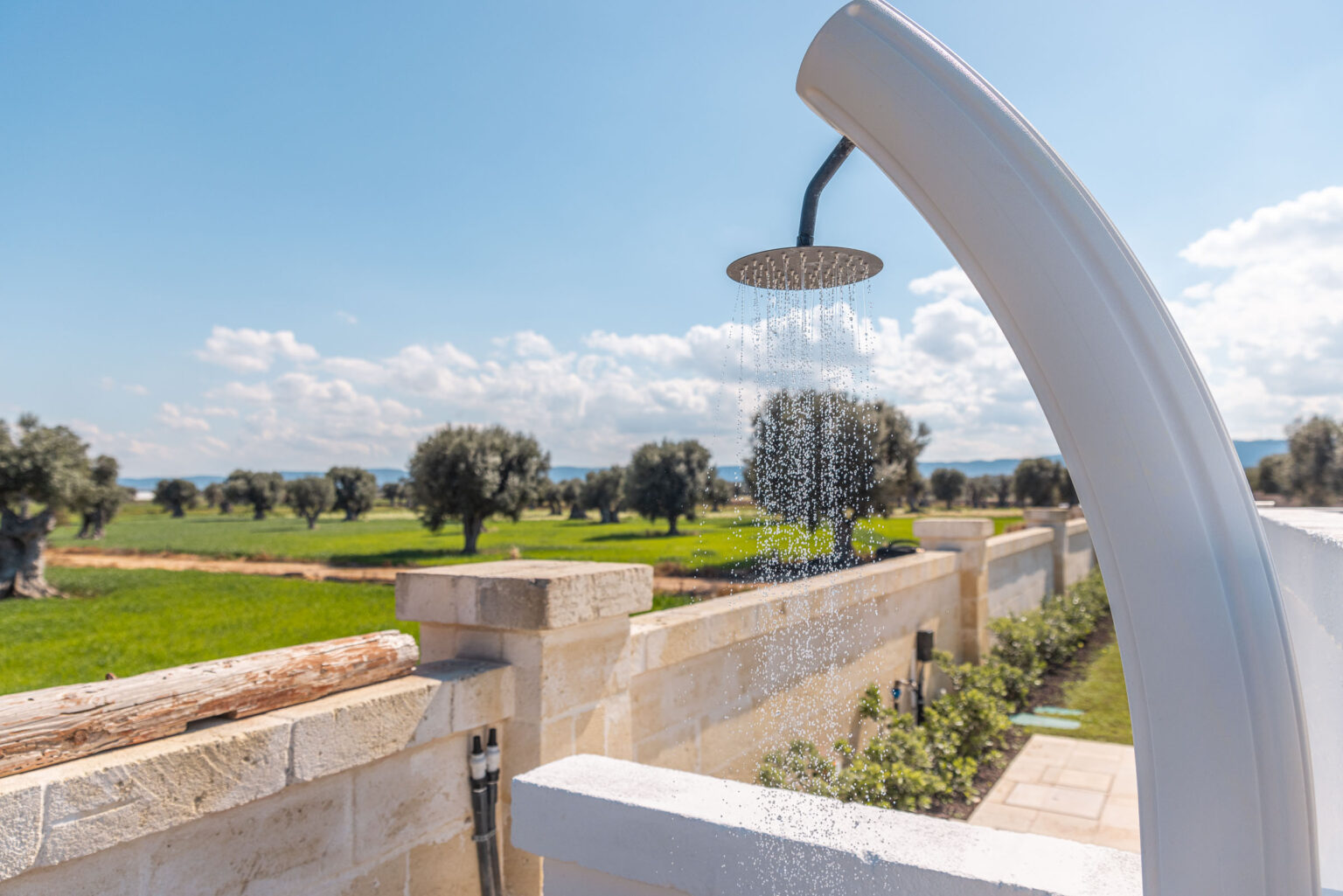 Outdoor shower with modern design, surrounded by lush green fields and olive trees under a clear blue sky, perfect for refreshing outdoor experiences. | Only on SopranoVillas