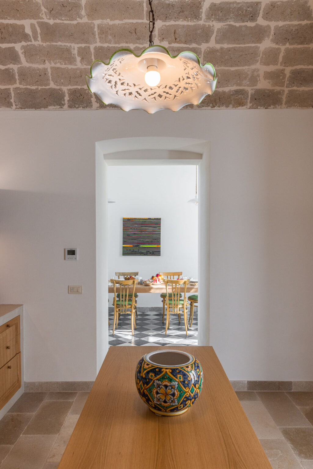 Modern dining area visible through an archway, featuring a colorful abstract painting on the wall and a wooden table set with chairs, surrounded by a bright, minimalist interior design. | Only on SopranoVillas