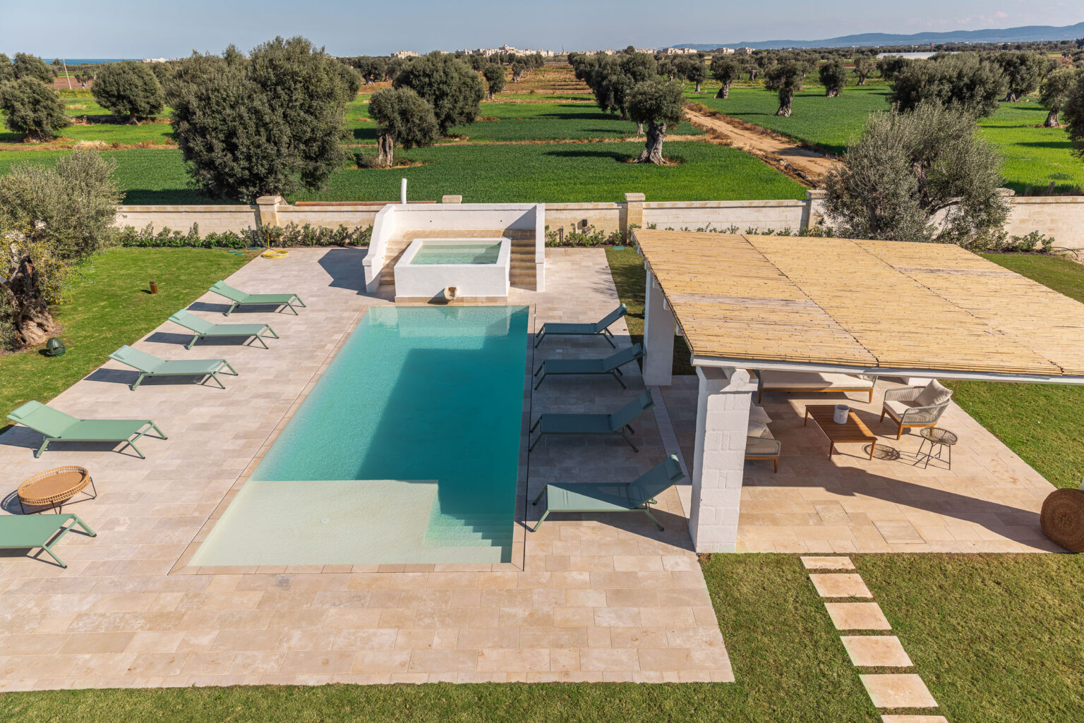 Luxurious outdoor pool area with sun loungers, a hot tub, and a shaded seating area surrounded by olive trees and lush greenery, showcasing a tranquil Mediterranean landscape. | Only on SopranoVillas