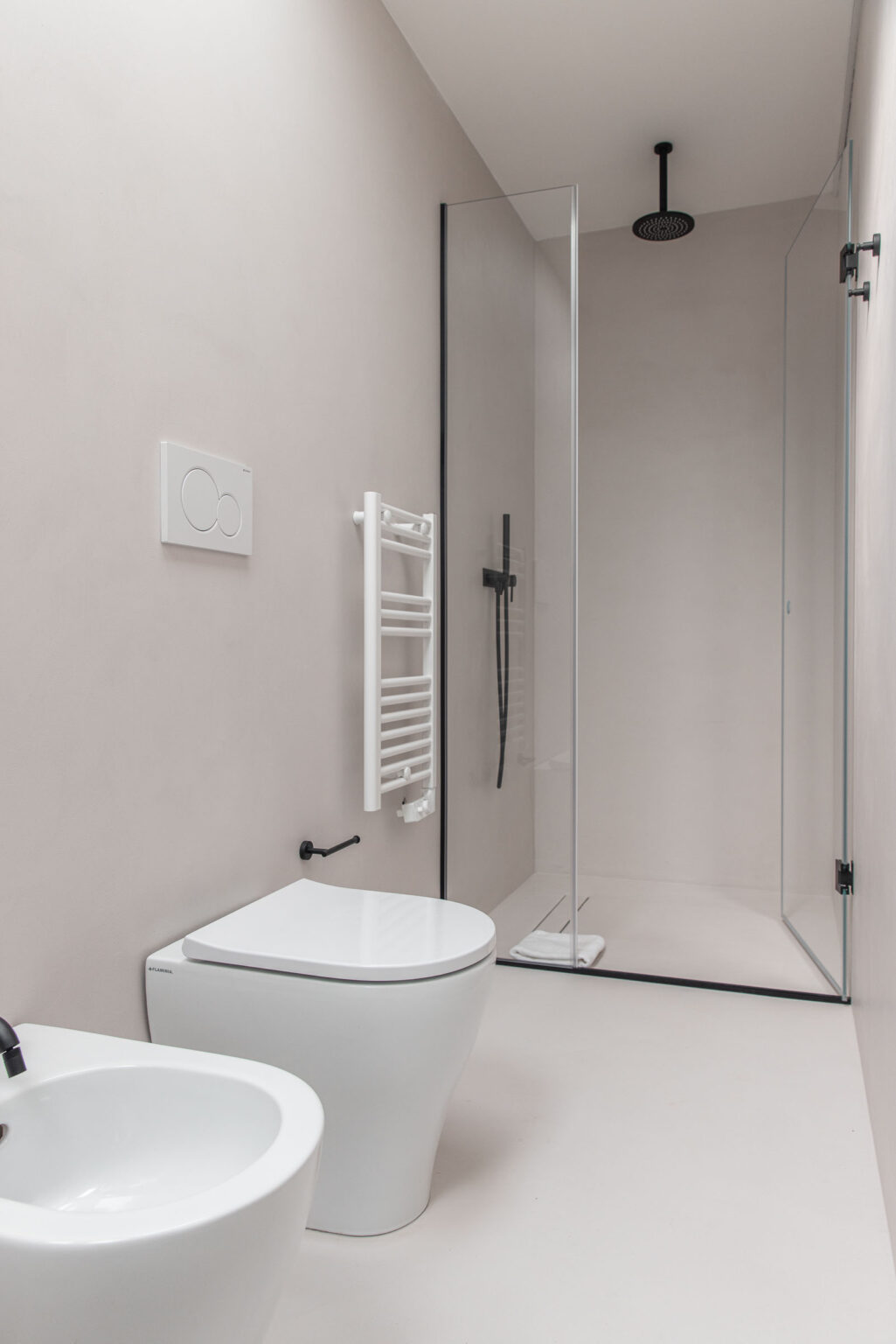 Modern bathroom interior featuring a glass shower enclosure, minimalist white toilet and bidet, heated towel rack, and sleek black fixtures against a neutral wall. Ideal for contemporary design inspiration. | Only on SopranoVillas