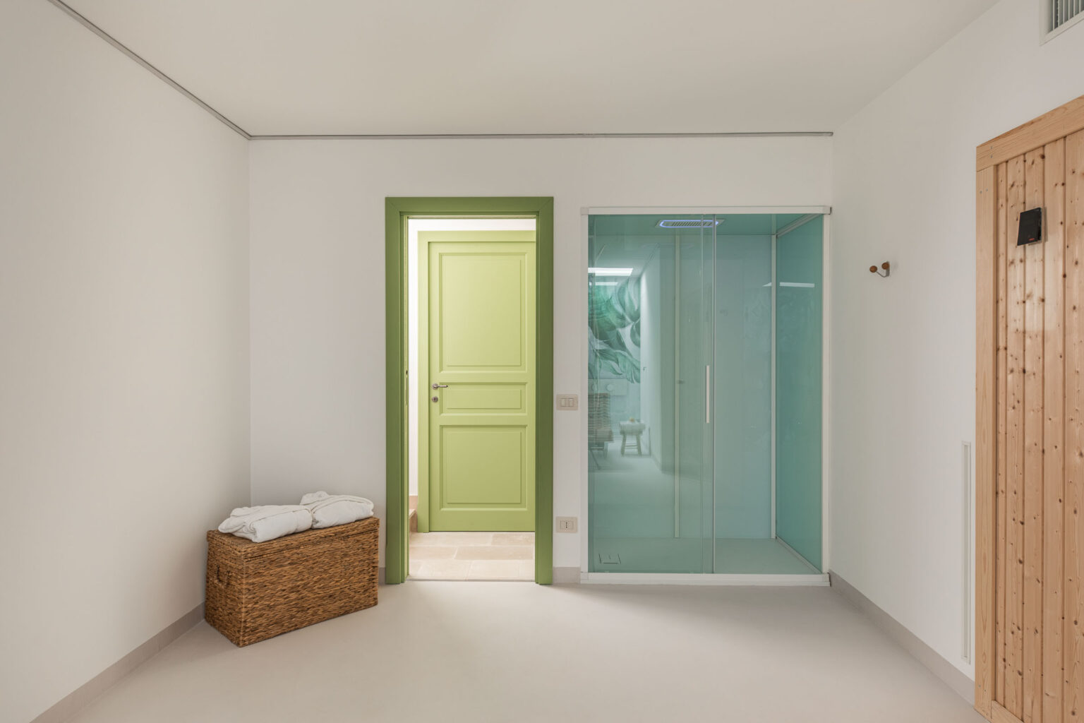 Modern bathroom interior featuring a glass shower enclosure, green door, and a wicker basket with towels. The walls are painted white, creating a clean and bright atmosphere. | Only on SopranoVillas