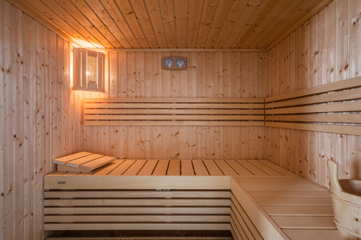 Interior of a wooden sauna featuring slatted benches, warm lighting, and temperature gauges on the wall, creating a relaxing atmosphere for wellness and relaxation. | Only on SopranoVillas