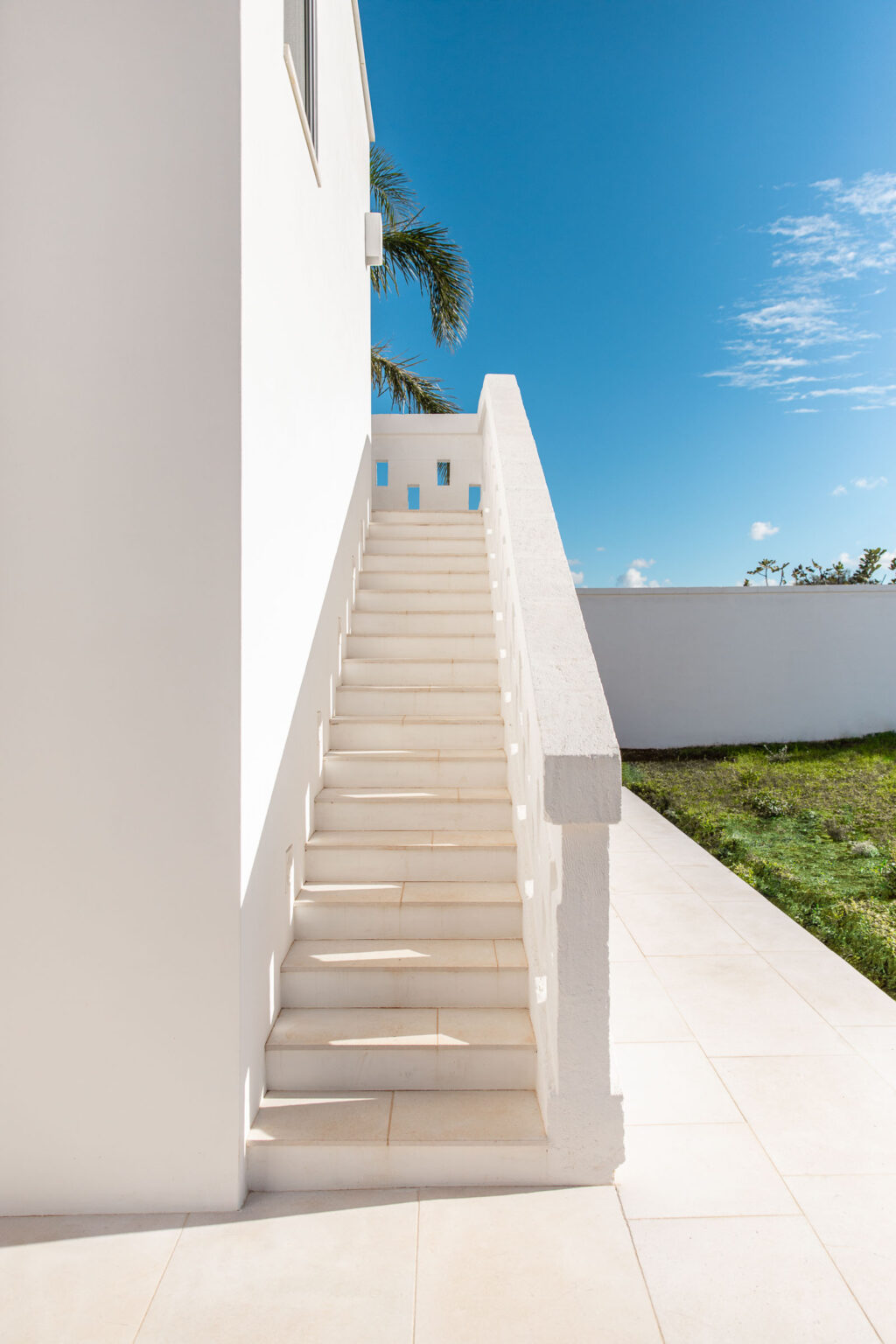 Modern white staircase leading to a bright outdoor space, surrounded by a minimalist architectural design and clear blue sky. | Only on SopranoVillas
