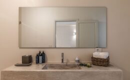 Modern bathroom sink with a minimalist design, featuring a large mirror, decorative toiletries, and organic elements like an apple and rosemary, enhancing the tranquil ambiance.