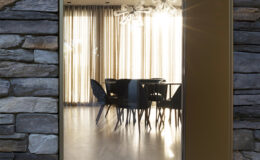 Modern entrance featuring a sleek glass door framed by natural stone, revealing a stylish dining area with elegant lighting and large windows that allow natural light to fill the space.