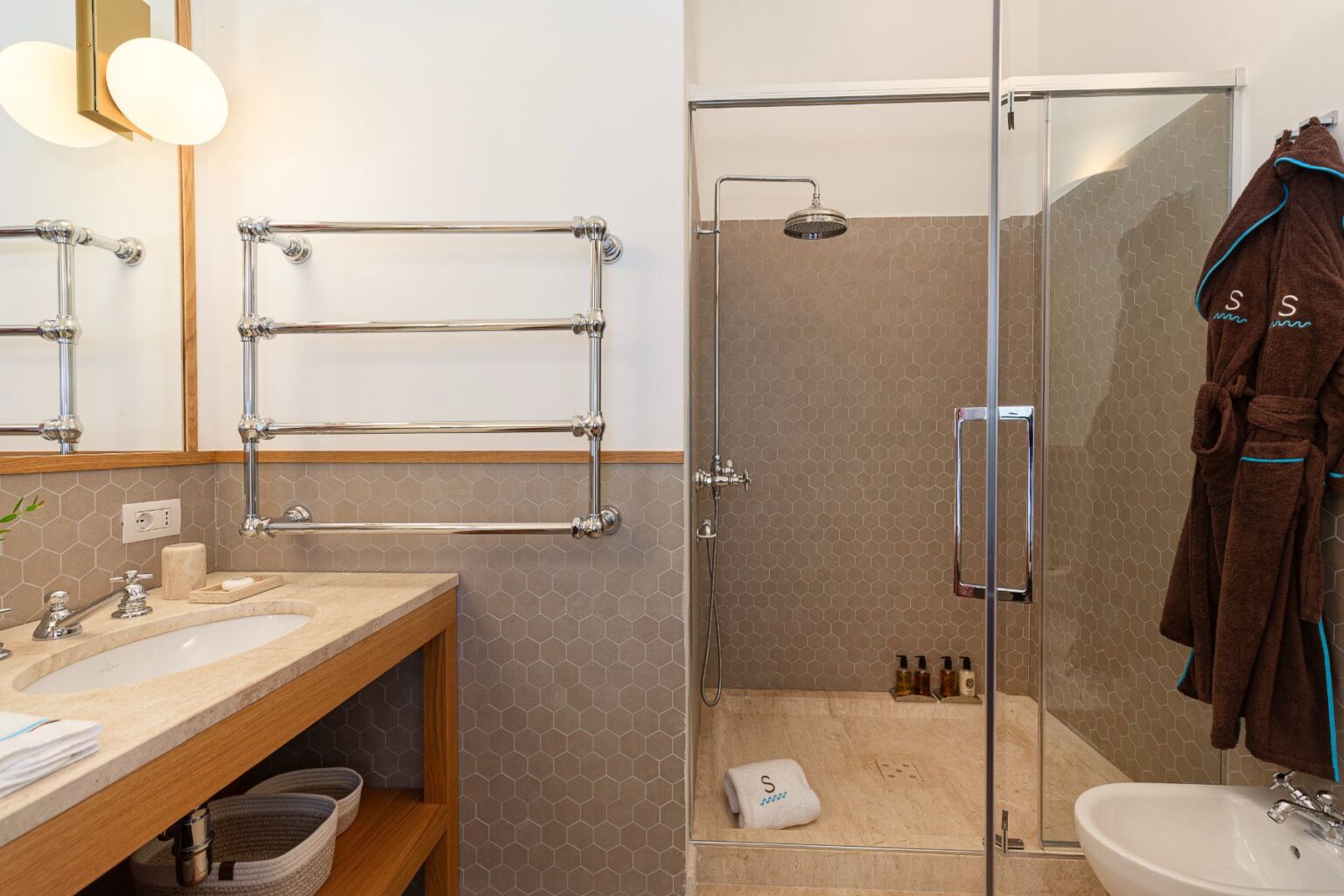 Modern bathroom featuring a glass shower enclosure, hexagonal tile accents, a stylish vanity with a stone sink, and chrome towel racks. Soft towels hang nearby, adding a touch of luxury to the space. | Only on SopranoVillas