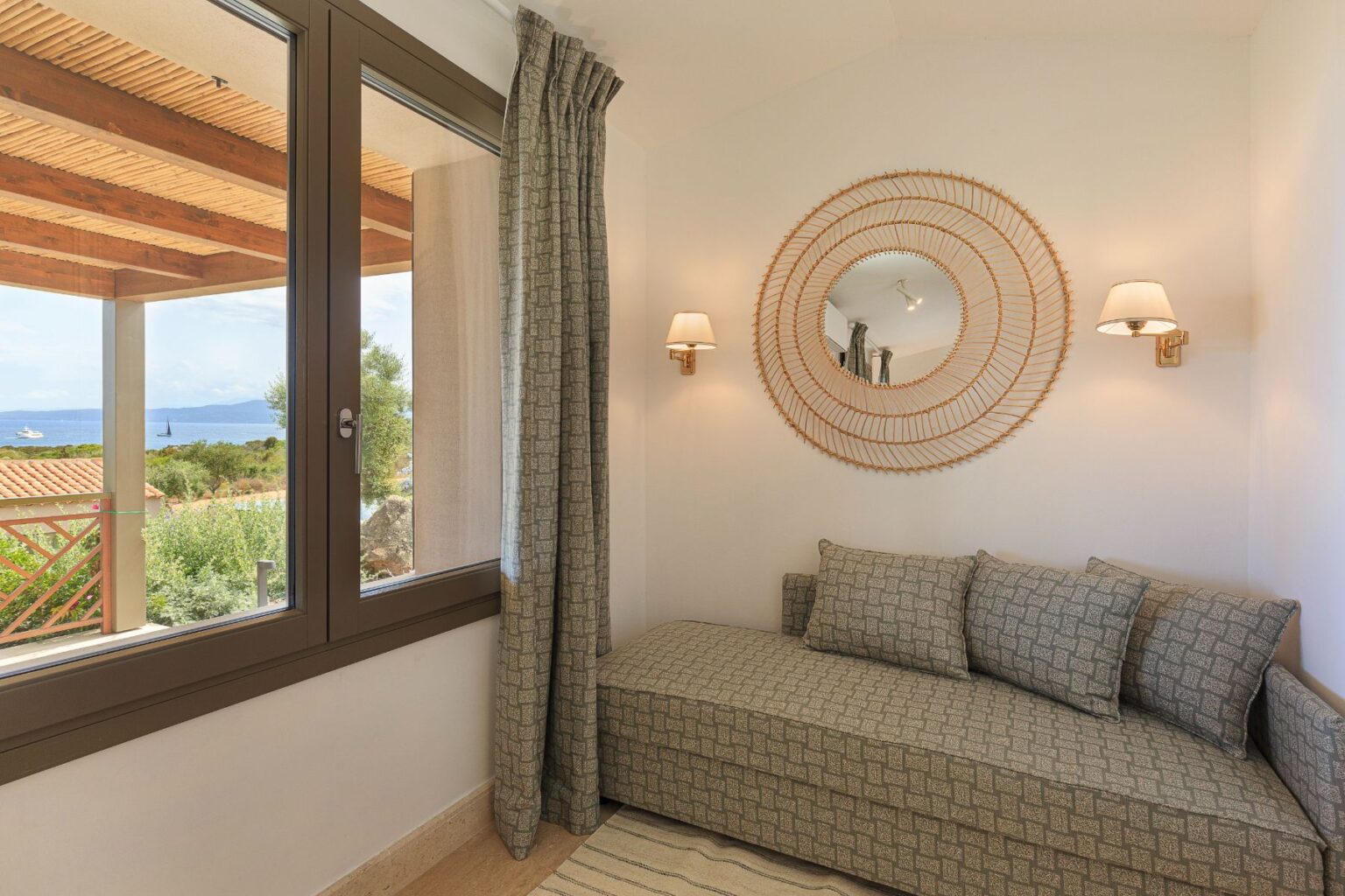 Cozy reading nook featuring a patterned daybed, decorative mirror, and soft lighting, with a scenic sea view visible through large windows. Ideal for relaxation and enjoying natural light. | Only on SopranoVillas