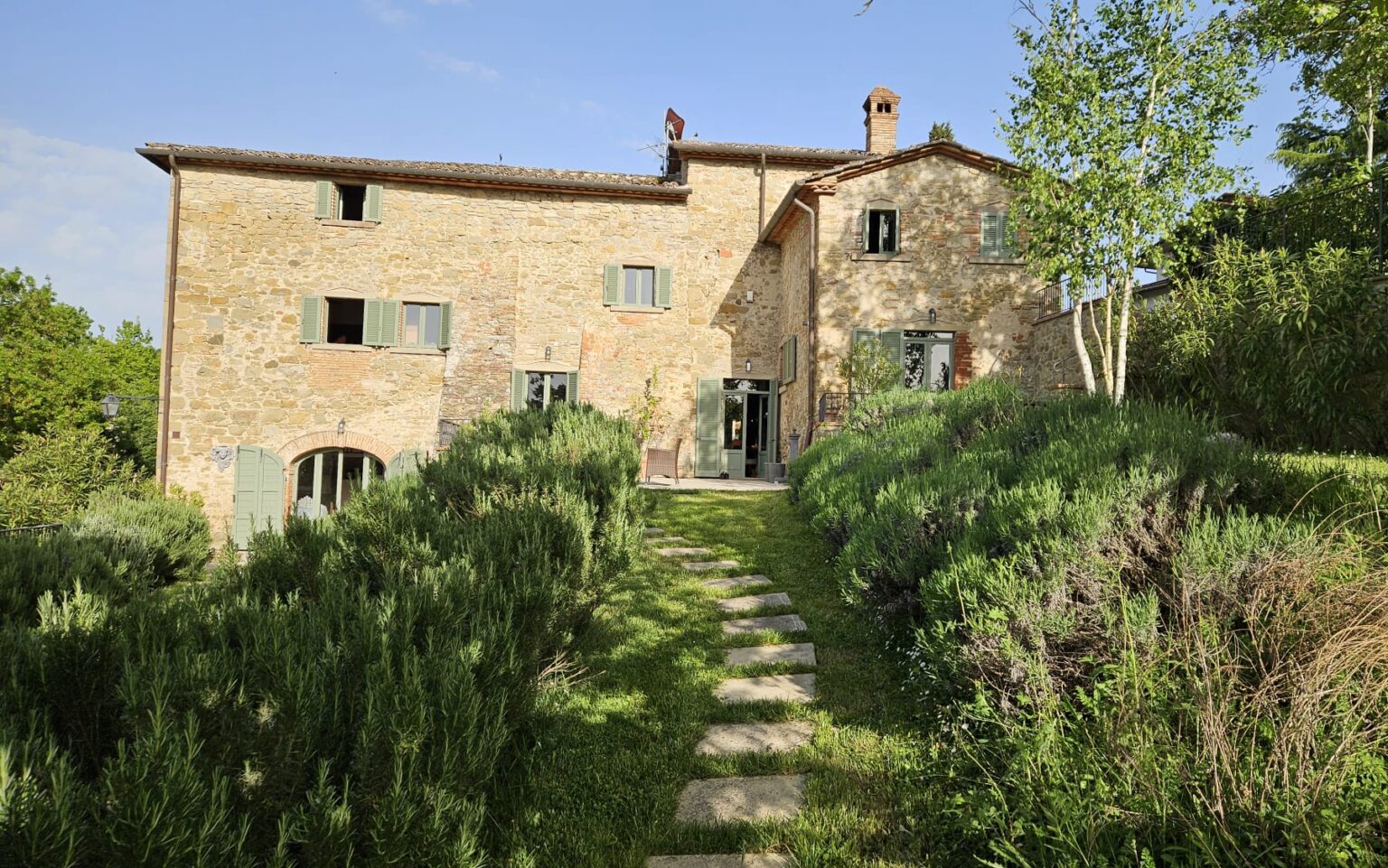 Charming rustic stone house surrounded by lush greenery and lavender, featuring a pathway leading to the entrance and a clear blue sky overhead. Ideal for a tranquil getaway in the countryside. | Only on SopranoVillas