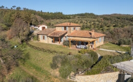 Aerial view of a charming stone villa with a terracotta roof, surrounded by lush greenery and rolling hills. The property features a spacious outdoor dining area and a well-maintained garden, showcasing the tranquility of rural living.