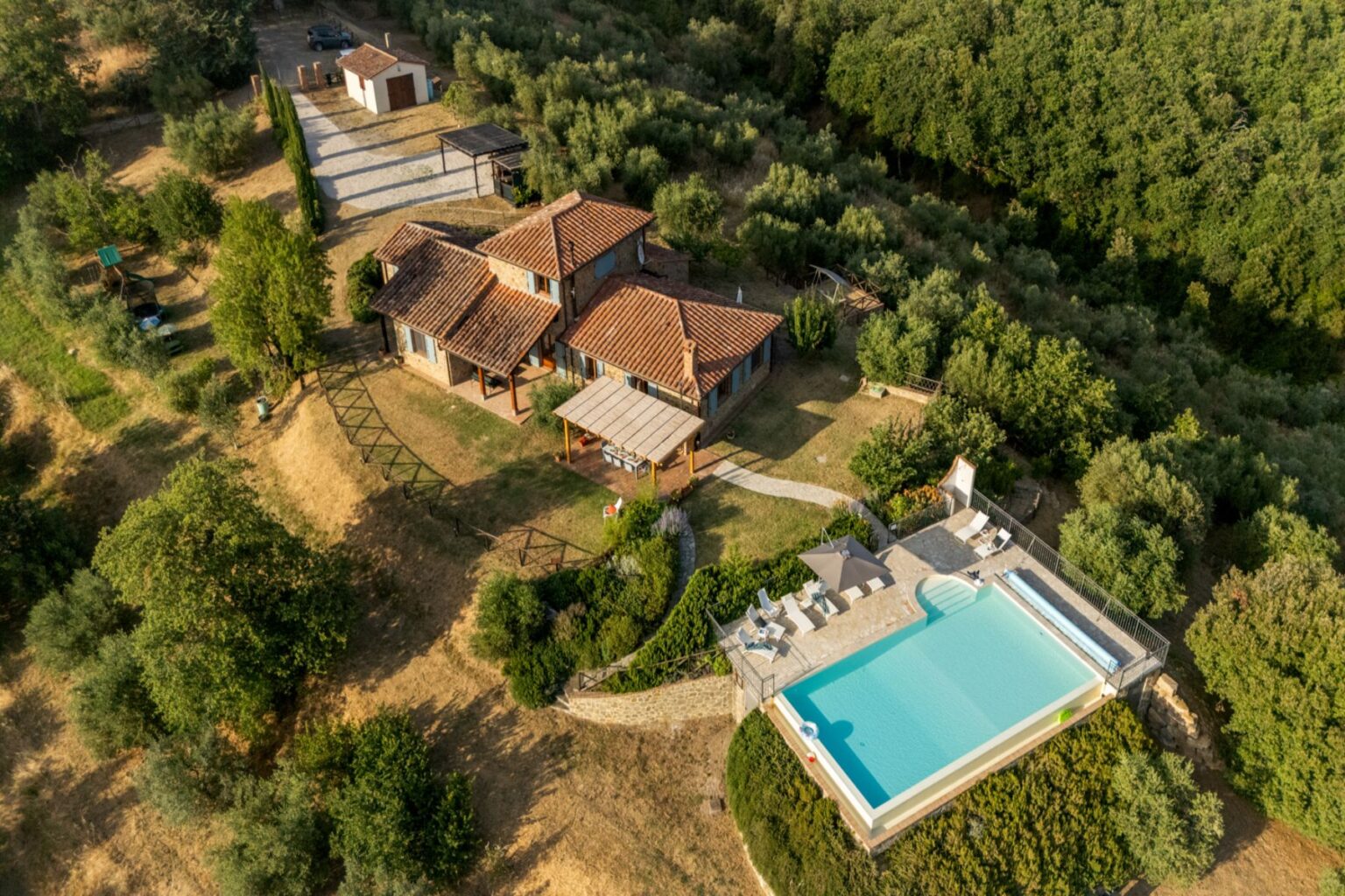 Aerial view of a scenic countryside villa surrounded by lush greenery, featuring a modern swimming pool and outdoor seating area, ideal for relaxation and luxury getaways. | Only on SopranoVillas