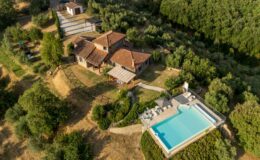 Aerial view of a scenic countryside villa surrounded by lush greenery, featuring a modern swimming pool and outdoor seating area, ideal for relaxation and luxury getaways.