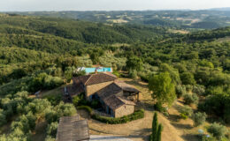 Aerial view of a charming rustic villa surrounded by lush green hills and olive groves, featuring a swimming pool and spacious outdoor areas, ideal for relaxation and nature retreats.
