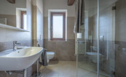 Modern bathroom interior featuring a sleek sink, toilet, and glass shower enclosure. The design includes natural light from a window, warm wood accents, and a towel rack, showcasing a stylish and functional space.