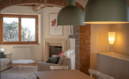 Cozy living room with a modern design featuring a white sofa, a minimalist coffee table, and a warm color palette. Natural light streams through large wooden windows, highlighting a stylish lamp and a classic fireplace. Exposed brick archways add character to the space, creating a welcoming atmosphere.