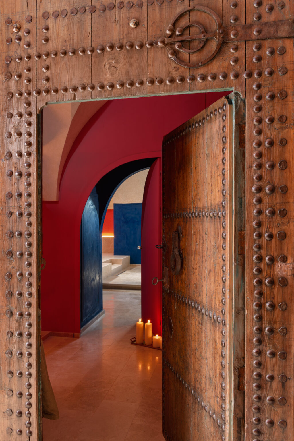 Intricately designed wooden doors open to a vibrant interior featuring rich red and blue walls, showcasing a blend of cultural aesthetics and modern design elements. | Only on SopranoVillas