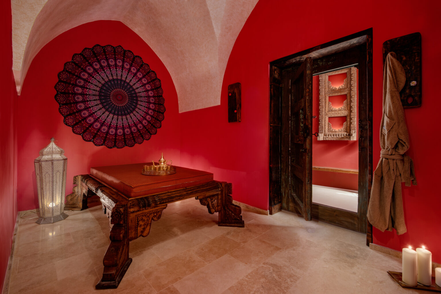 Interior of a vibrant red room featuring a decorative wall hanging, a wooden table, candles, and an inviting atmosphere. The space is elegantly designed, showcasing traditional decor and a warm ambiance, ideal for relaxation or meditation. | Only on SopranoVillas