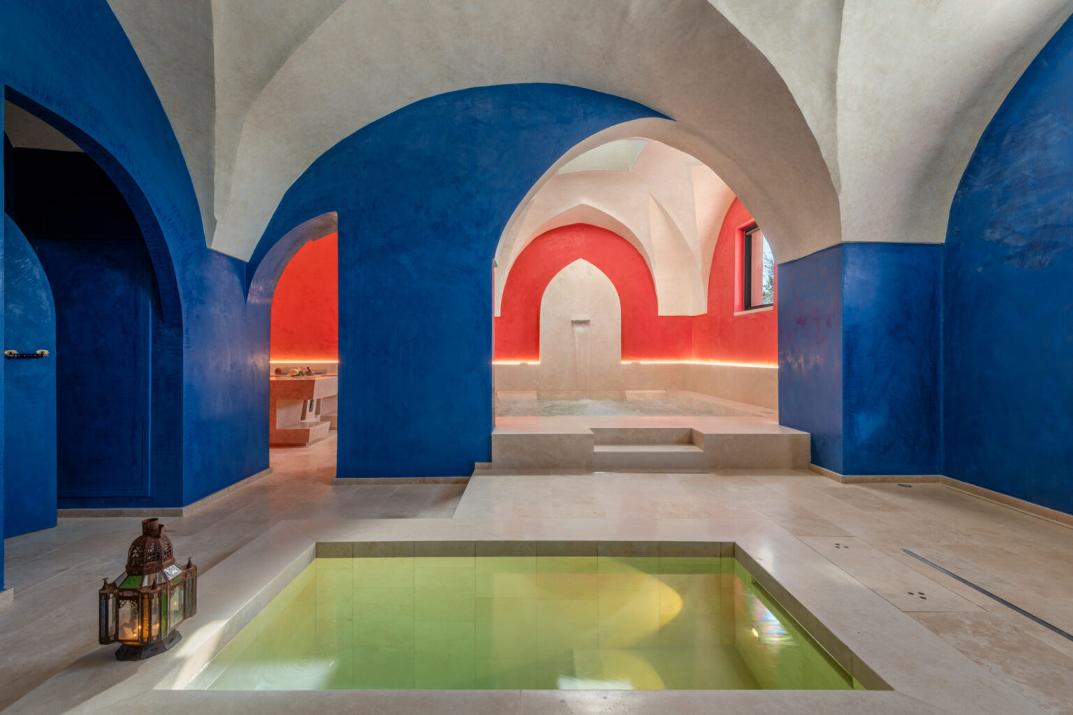 Luxurious spa interior featuring blue and red arched walls, a serene green pool, and elegant lighting, designed for relaxation and wellness. | Only on SopranoVillas