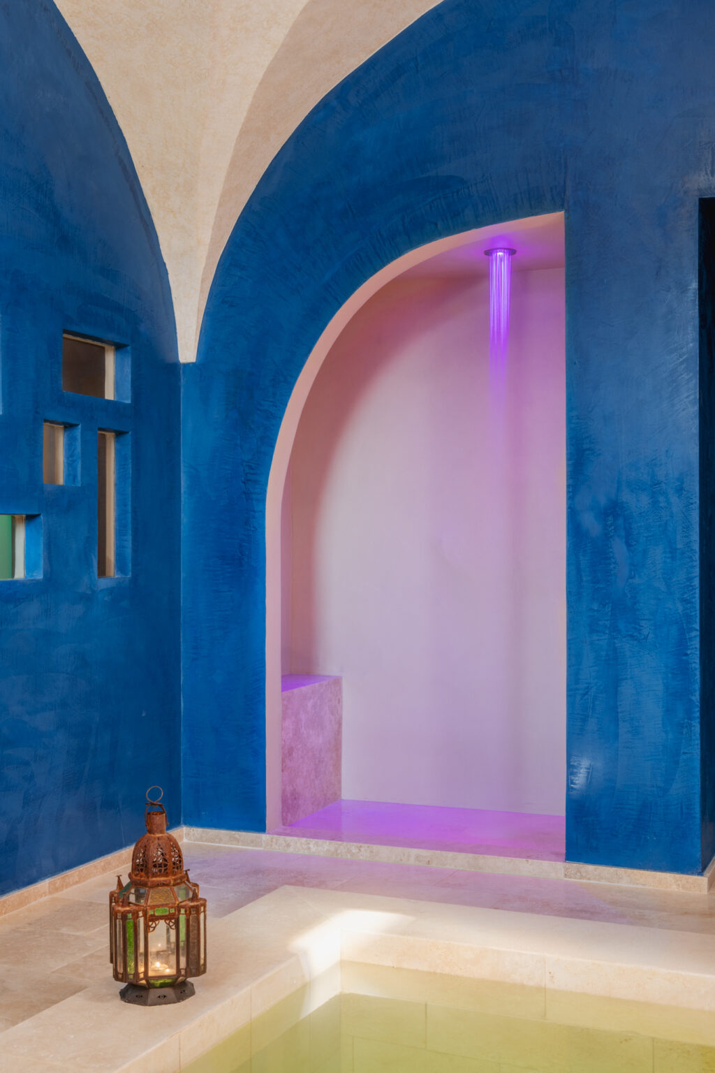 Interior view of a stylish architectural space featuring a blue wall with an arched opening and soft pink tones, illuminated by subtle lighting. | Only on SopranoVillas
