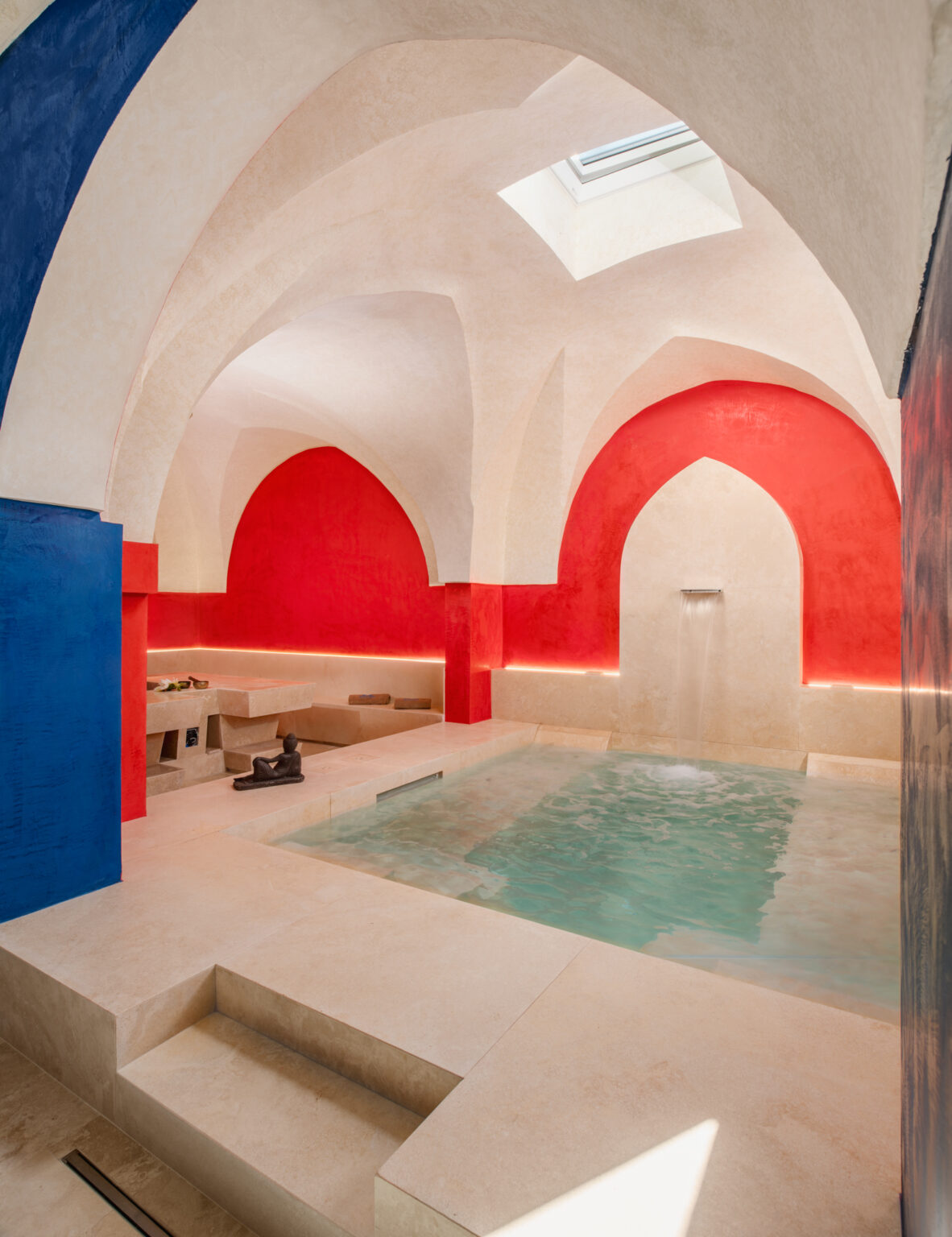 Interior view of a luxurious spa featuring a serene water pool, elegantly designed arches, and vibrant red and blue wall accents, creating a tranquil atmosphere for relaxation and wellness. | Only on SopranoVillas