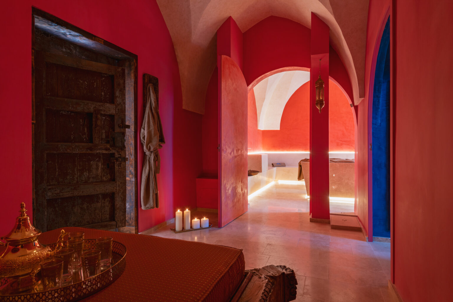 Interior view of a vibrant spa or wellness center featuring red walls, arches, and soft lighting, with candles and decorative elements creating a calming atmosphere. | Only on SopranoVillas