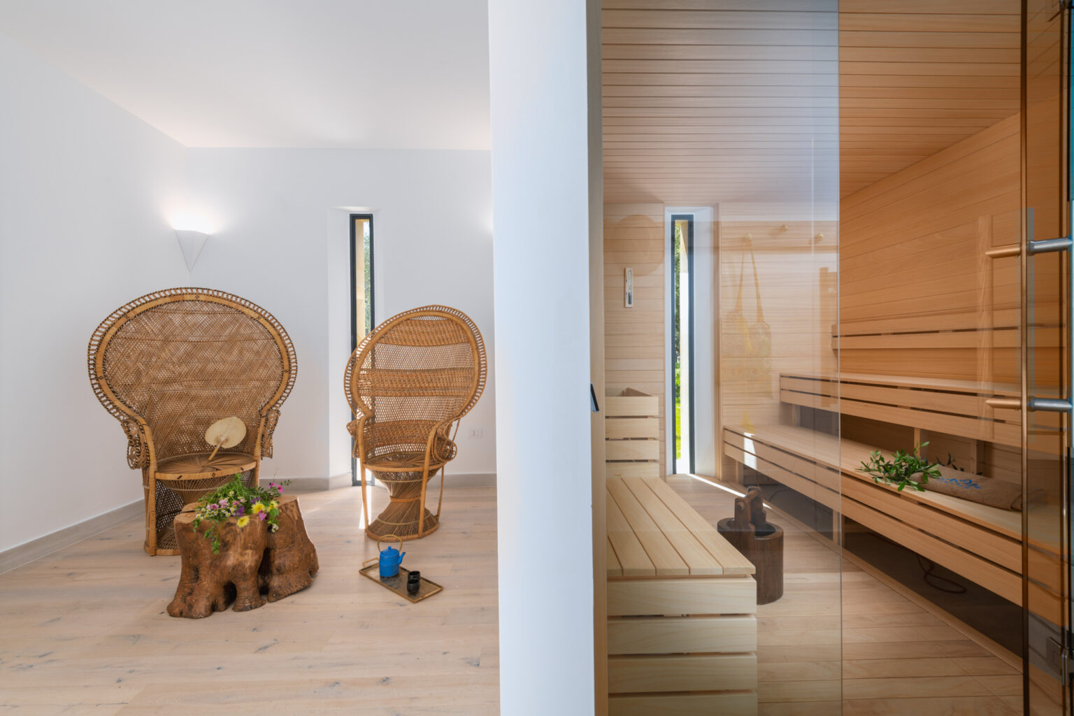 Modern wellness space featuring two stylish wicker chairs and a wooden sauna, designed for relaxation and tranquility. Natural light streams through narrow windows, enhancing the serene atmosphere. | Only on SopranoVillas