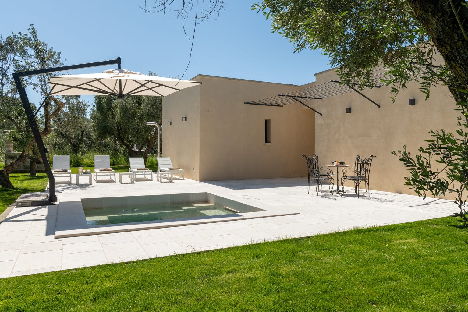 Modern villa exterior with a private pool, sun loungers, and outdoor seating area surrounded by lush greenery and olive trees. Ideal for relaxation and leisure. | Only on SopranoVillas