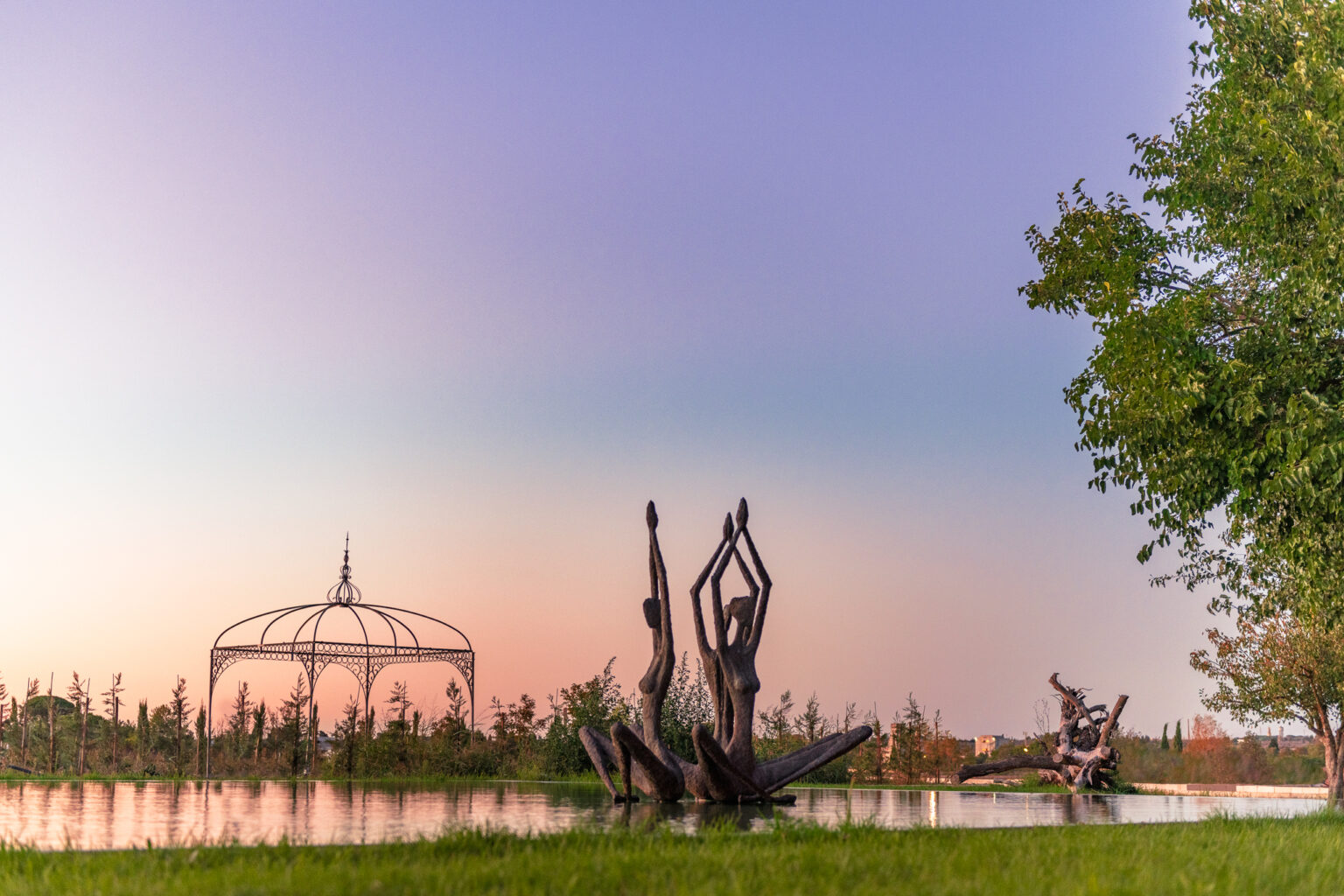 Sculptures of dancing figures surrounded by a serene pond at sunset, with a decorative gazebo in the background and lush trees framing the scene. | Only on SopranoVillas