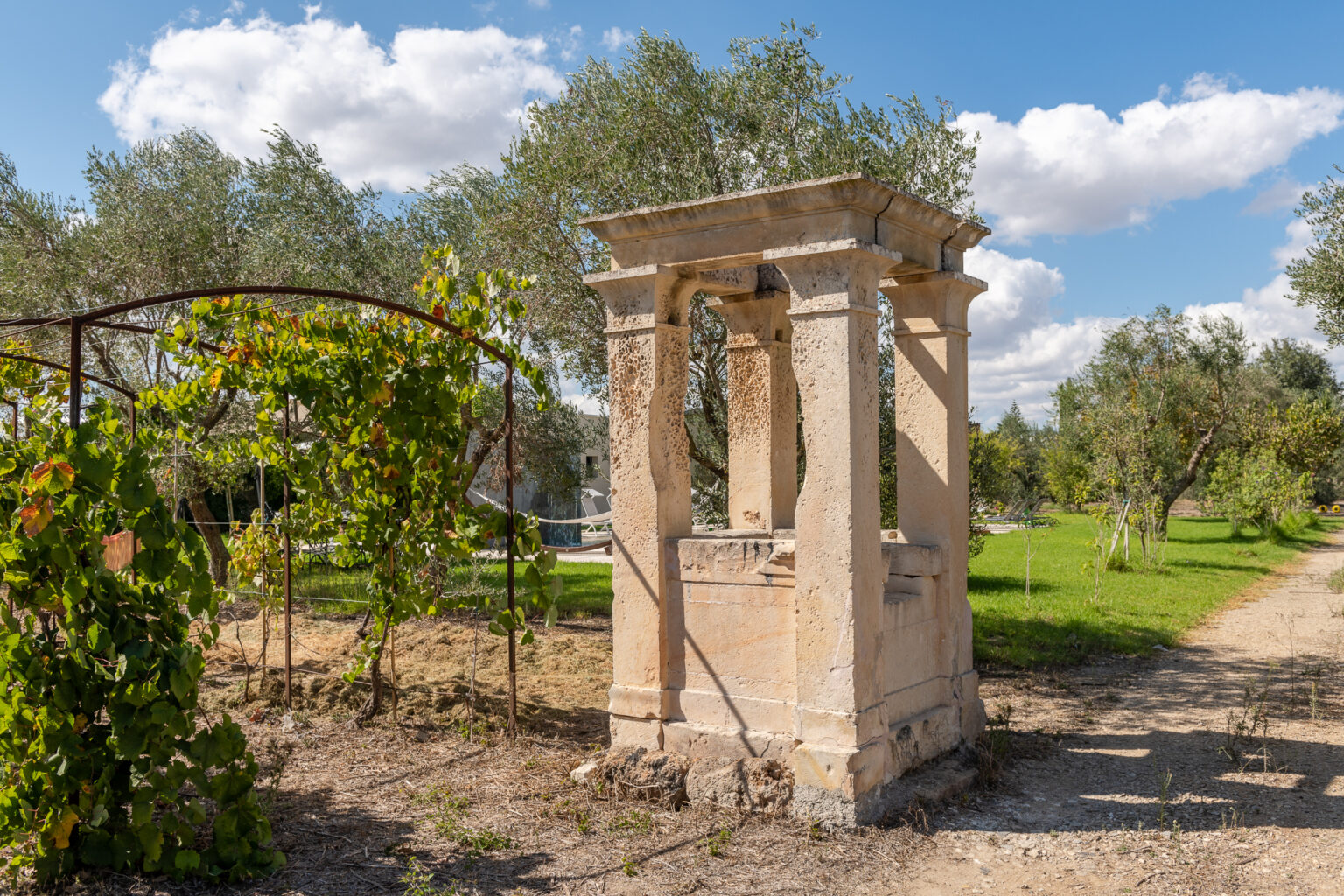 Ruins of an ancient stone structure surrounded by lush greenery and olive trees under a blue sky with fluffy clouds. | Only on SopranoVillas
