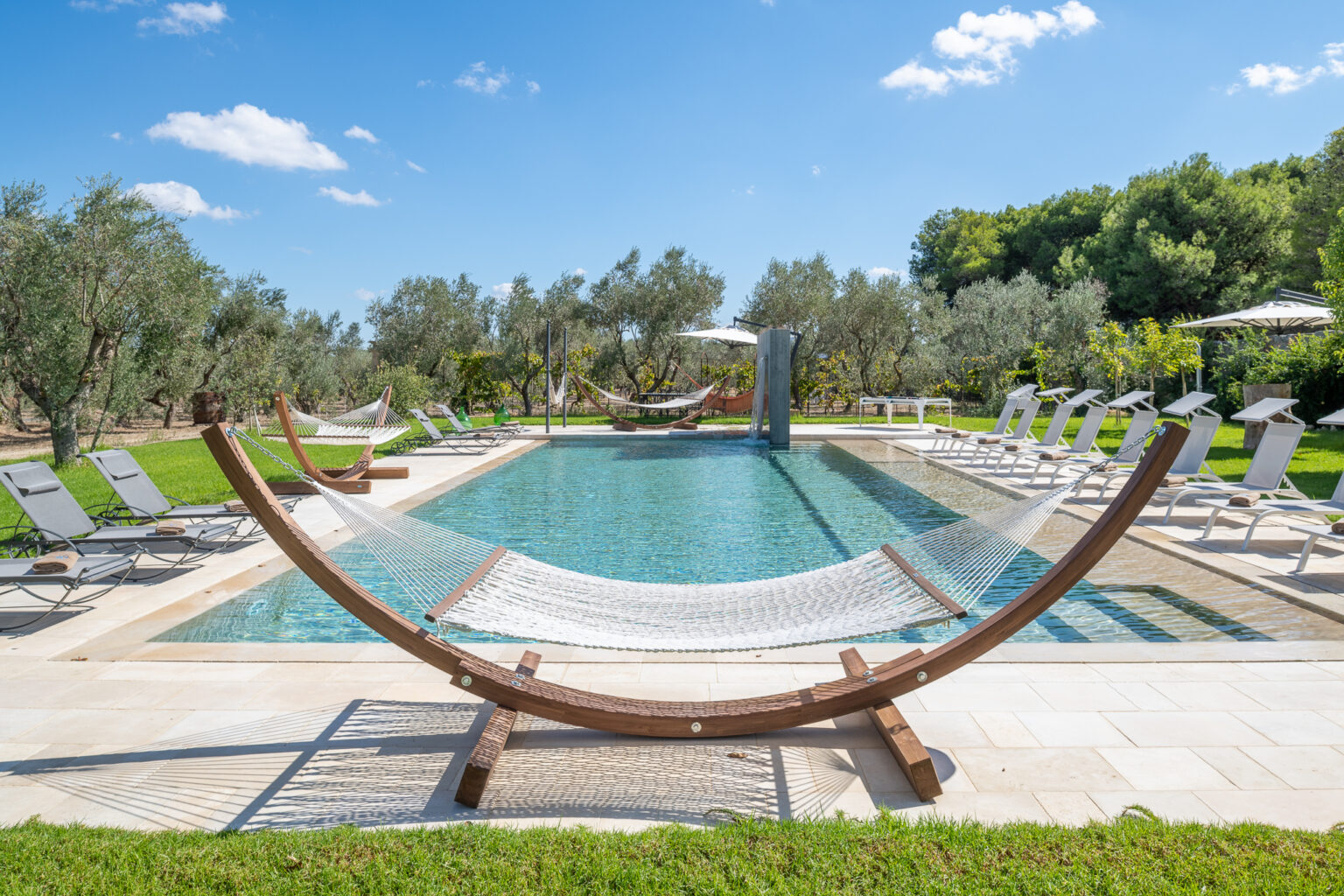 Relaxing outdoor pool area featuring a hammock, sun loungers, and olive trees under a bright blue sky. | Only on SopranoVillas