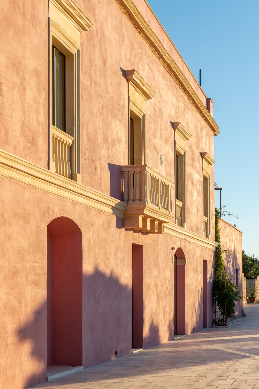 Historic pink building facade with ornate balcony and arched windows, bathed in warm sunlight. | Only on SopranoVillas