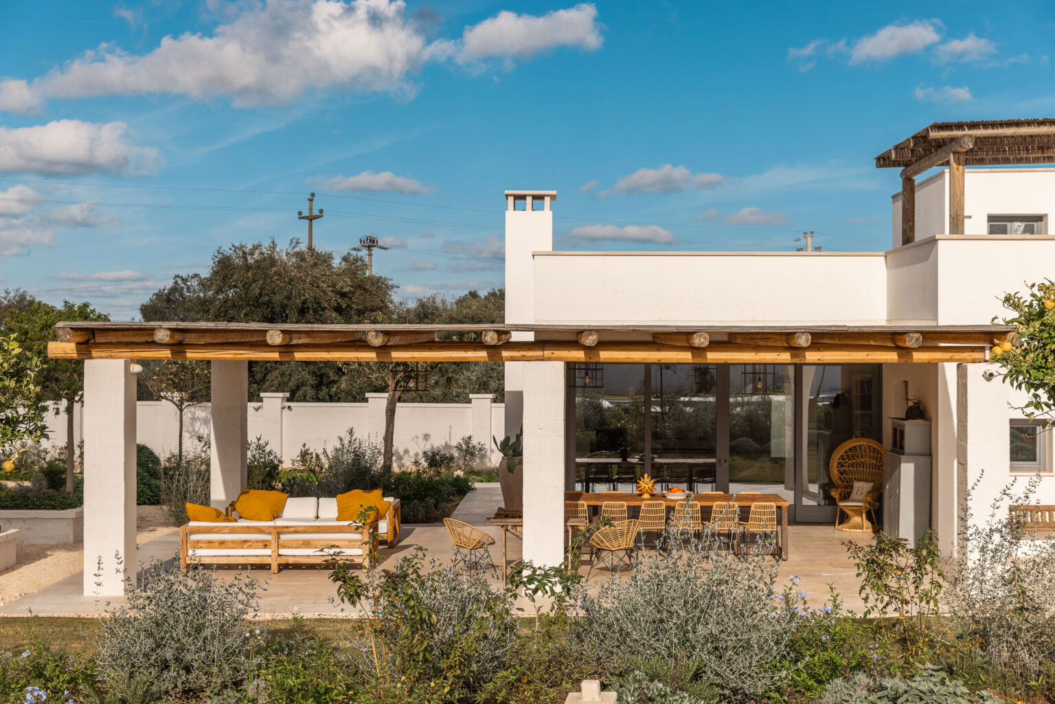 Modern house exterior with a spacious patio, featuring comfortable outdoor seating and a dining area, surrounded by lush greenery and a clear blue sky. Ideal for outdoor living and relaxation. | Only on SopranoVillas