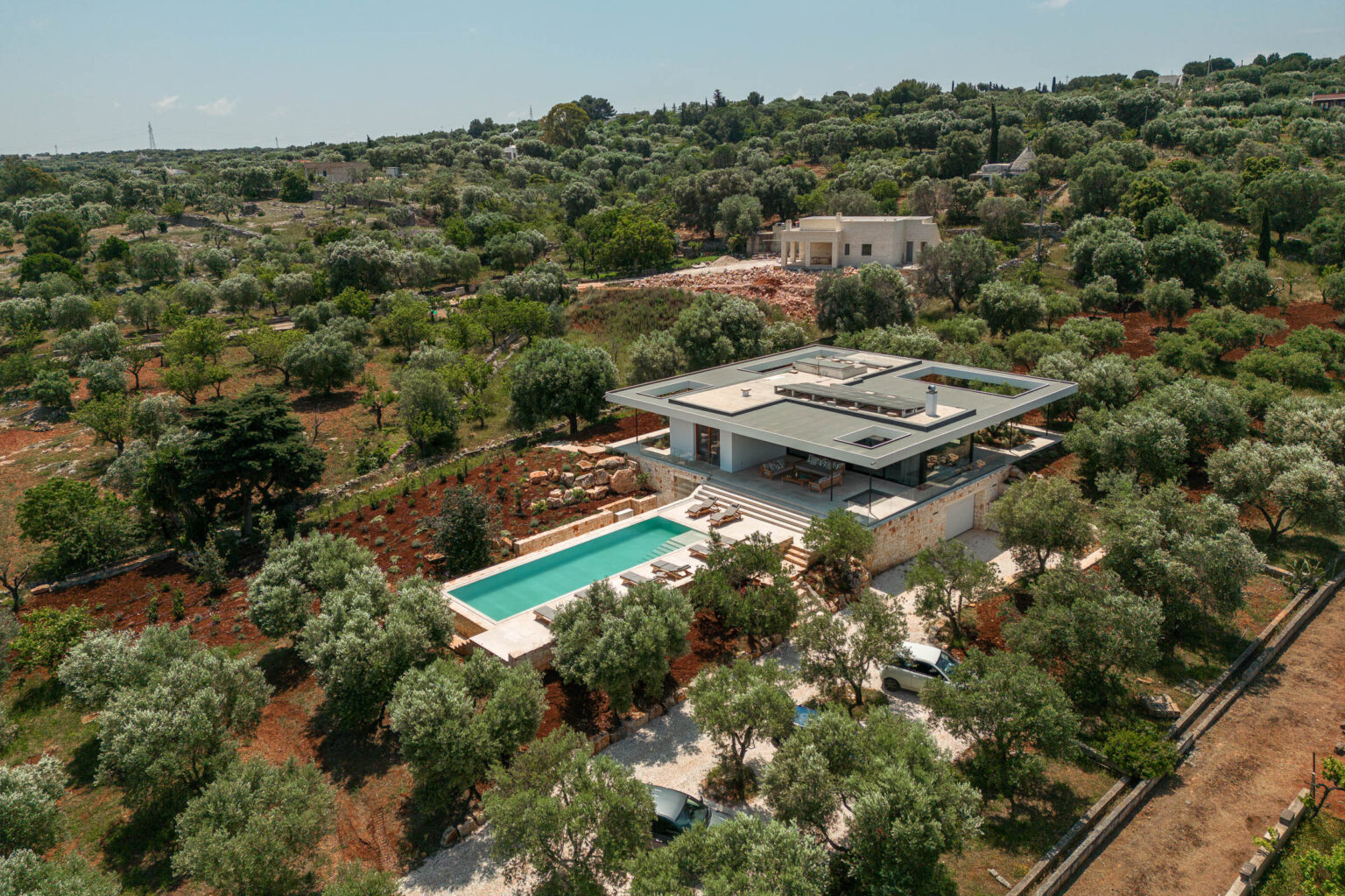 Modern villa with a swimming pool surrounded by olive trees and lush greenery in a tranquil landscape. The image showcases the contemporary architectural design and outdoor living space, emphasizing a serene and luxurious lifestyle. | Only on SopranoVillas