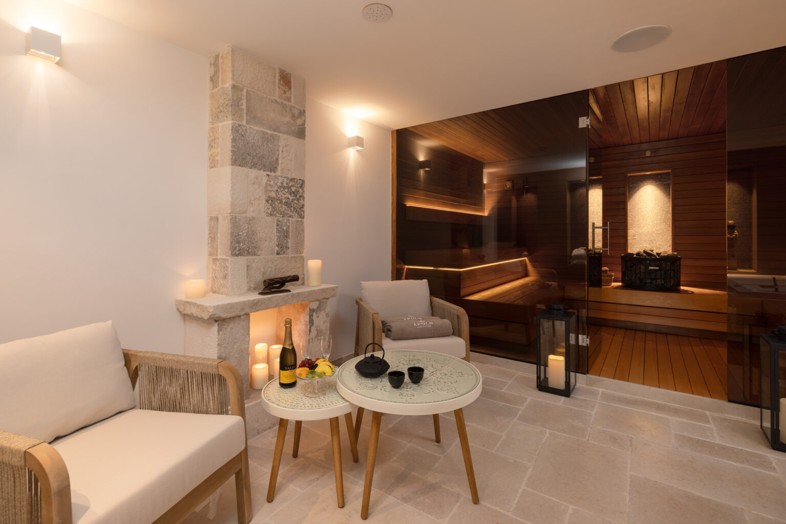 Cozy spa lounge area featuring comfortable seating, a small table with refreshments, and a view of a sauna, illuminated by soft lighting for a relaxing atmosphere. | Only on SopranoVillas