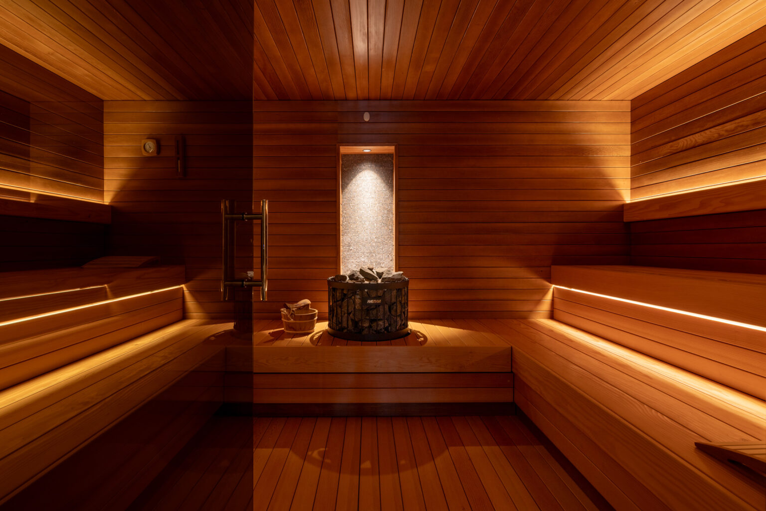 Interior view of a wooden sauna featuring benches, ambient lighting, and a stone heater, creating a relaxing atmosphere for wellness and relaxation. | Only on SopranoVillas