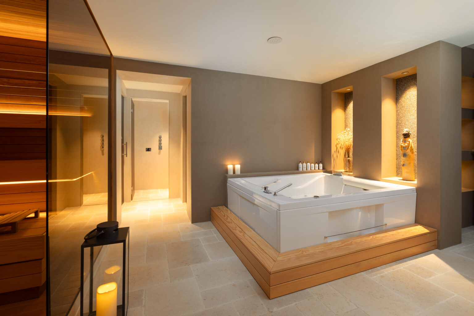Modern bathroom interior featuring a luxurious jacuzzi tub, warm lighting, and minimalist design elements. The space includes wood accents, a glass shower enclosure, and stylish wall niches for decorative items. | Only on SopranoVillas