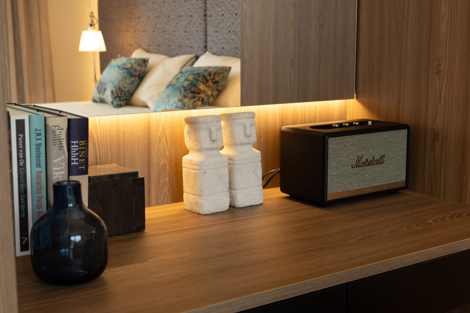 Modern bedroom decor featuring a wooden desk with a vintage-style speaker, decorative books, a blue vase, and white sculptures, illuminated by soft LED lighting. | Only on SopranoVillas