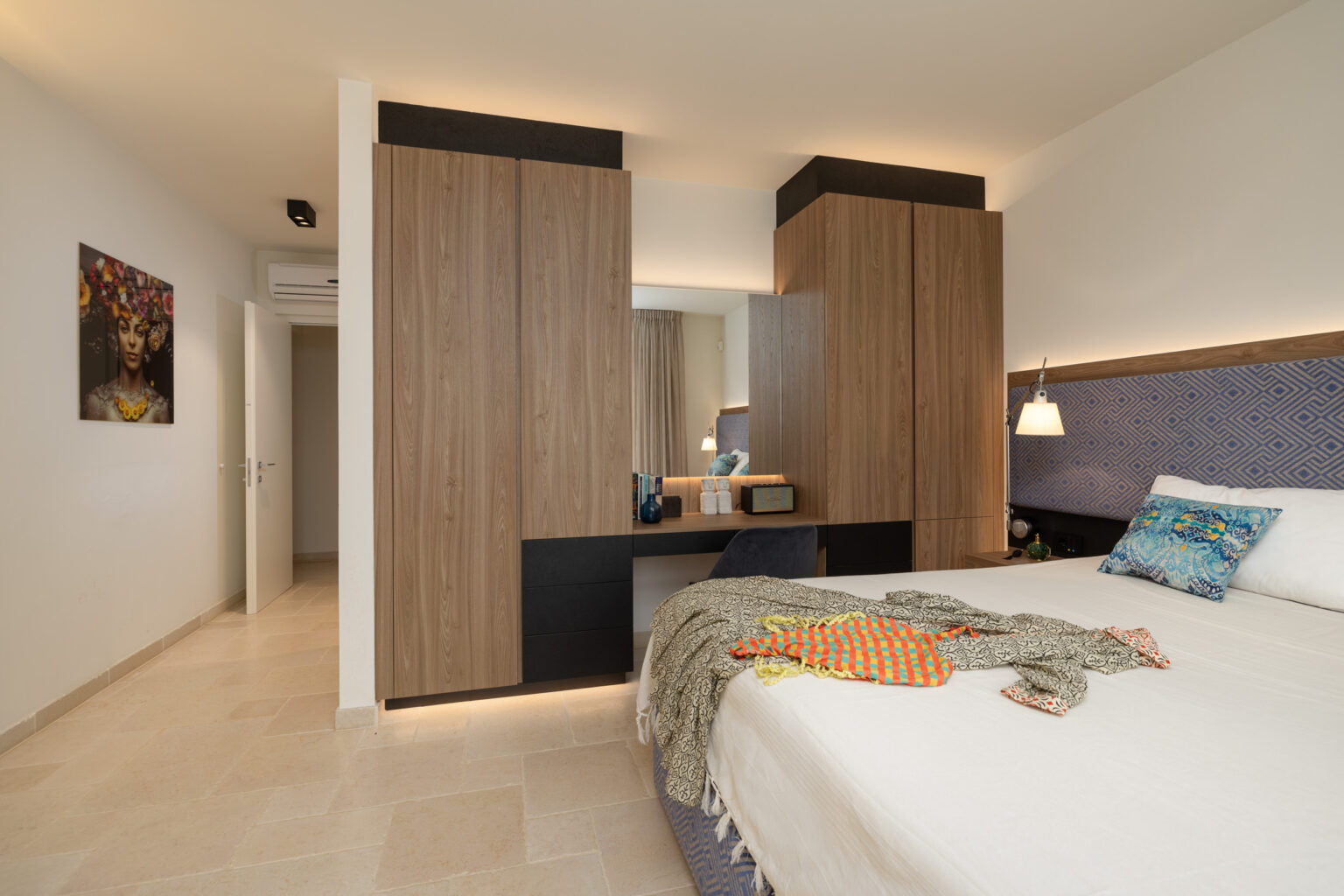 Modern hotel room featuring a queen-sized bed with a decorative throw, stylish wooden cabinetry, and contemporary lighting. The space includes a mirror and artwork on the wall, creating a cozy and inviting atmosphere. | Only on SopranoVillas