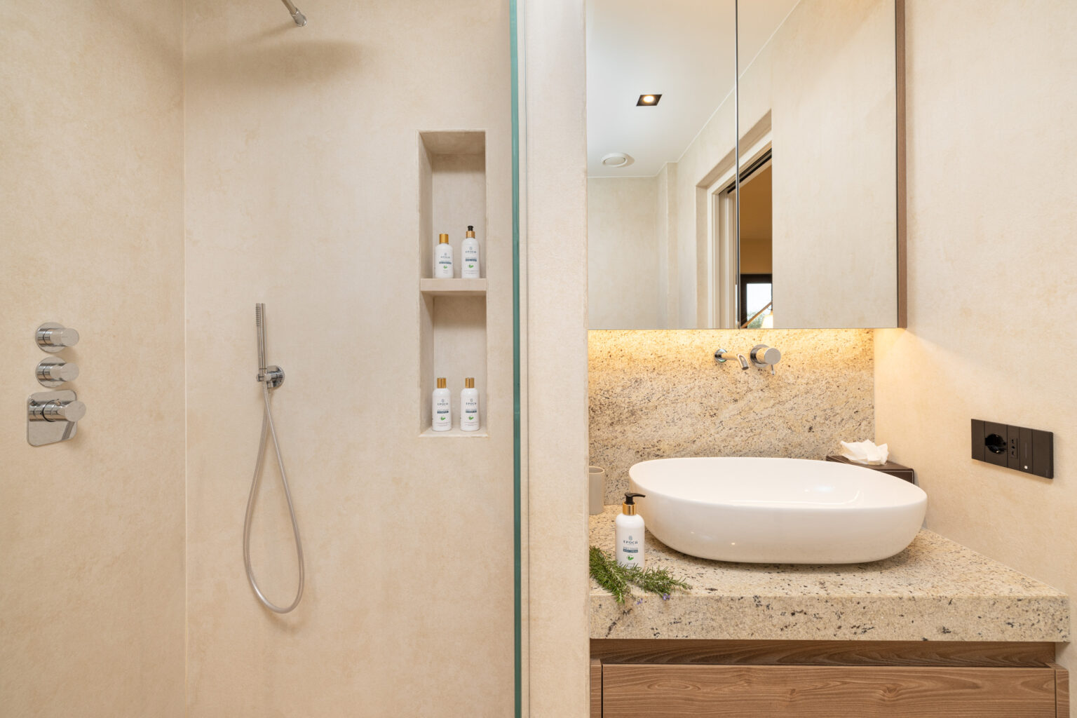 Modern bathroom design featuring a spacious shower with a sleek showerhead, built-in shelving for toiletries, and a stylish vanity with a round basin and warm lighting. | Only on SopranoVillas
