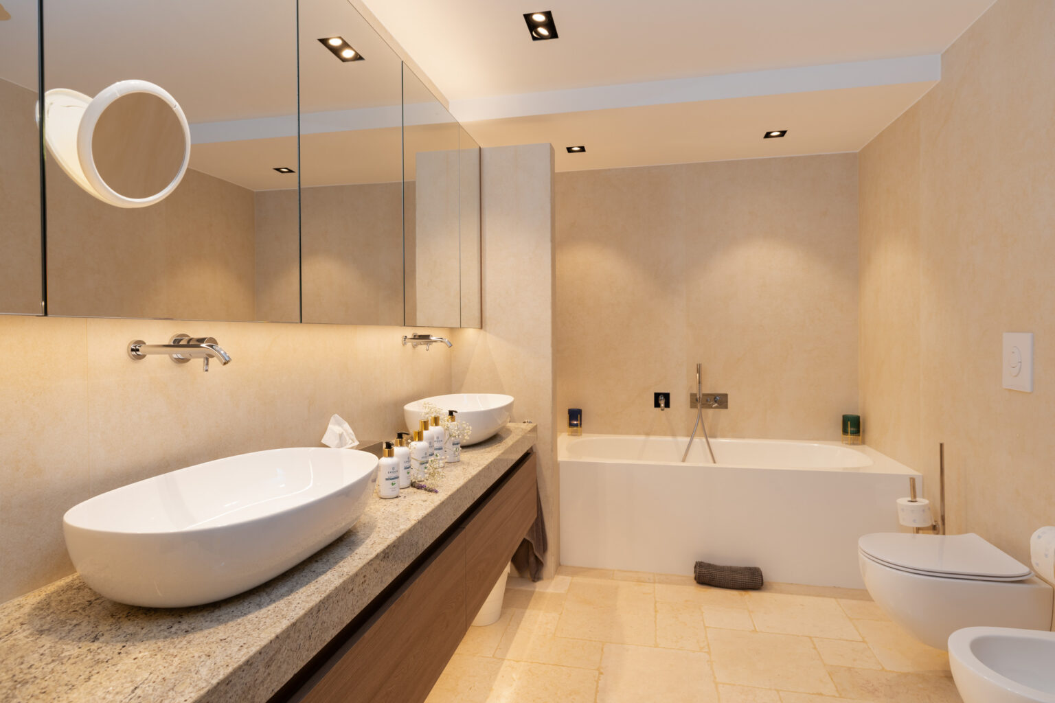 Modern bathroom interior featuring a double sink vanity with elegant bowls, a spacious bathtub, and contemporary fixtures. The warm-toned walls and sleek lighting create a luxurious atmosphere, complemented by a minimalist design. | Only on SopranoVillas